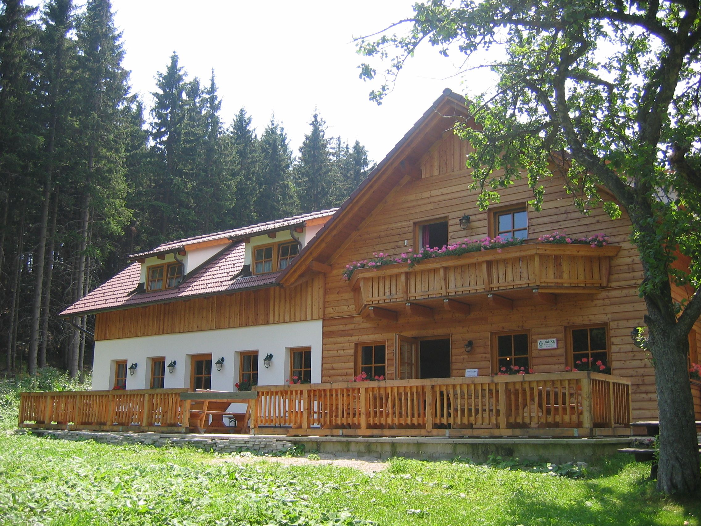 A rustic wooden mountain hut with balcony and terrace, surrounded by trees.
