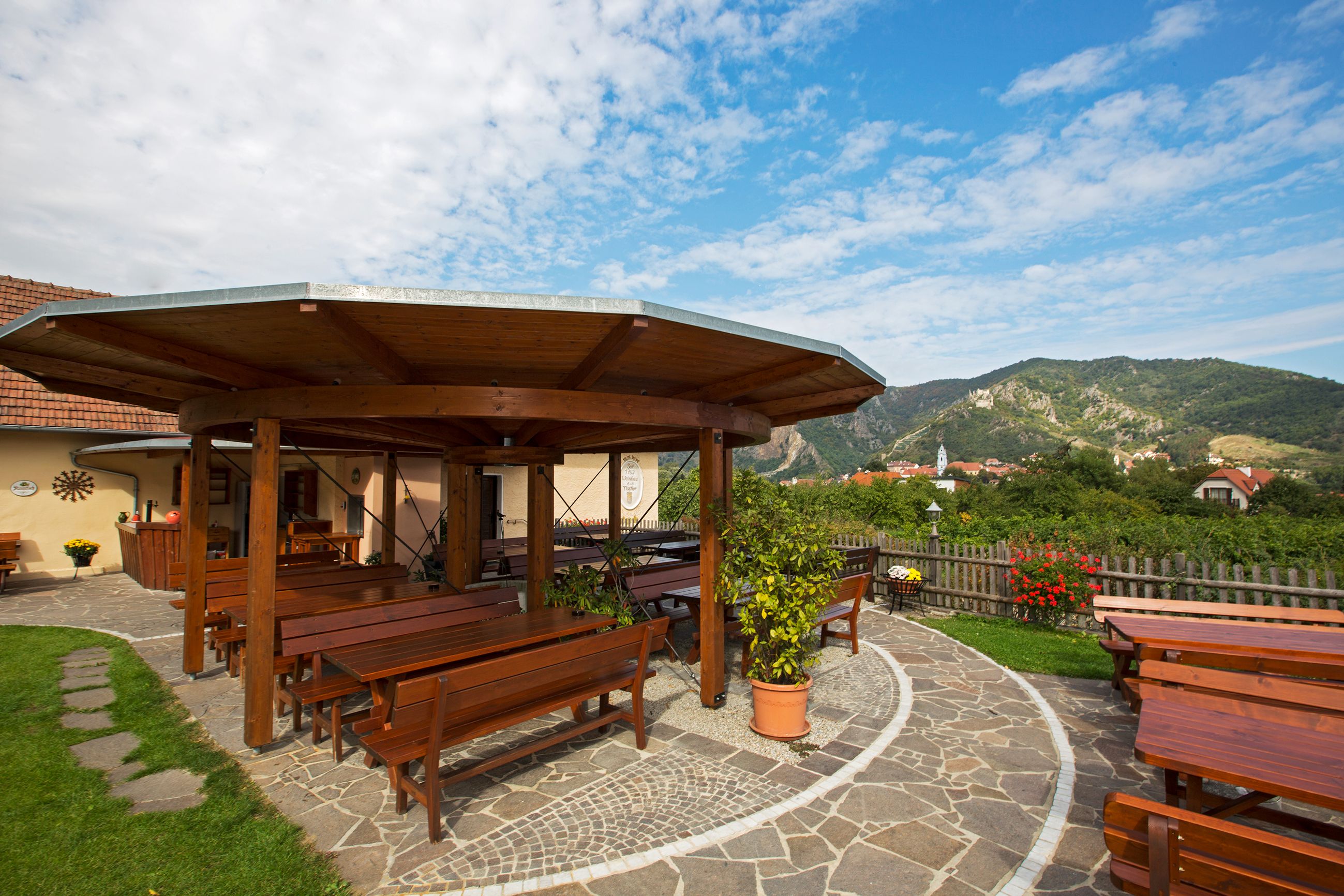 A guest garden with wooden tables and benches, surrounded by green countryside and mountains in the background.