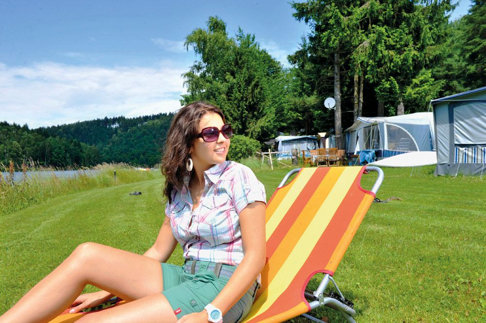 Woman relaxing on a deck chair at the campsite by the lake.