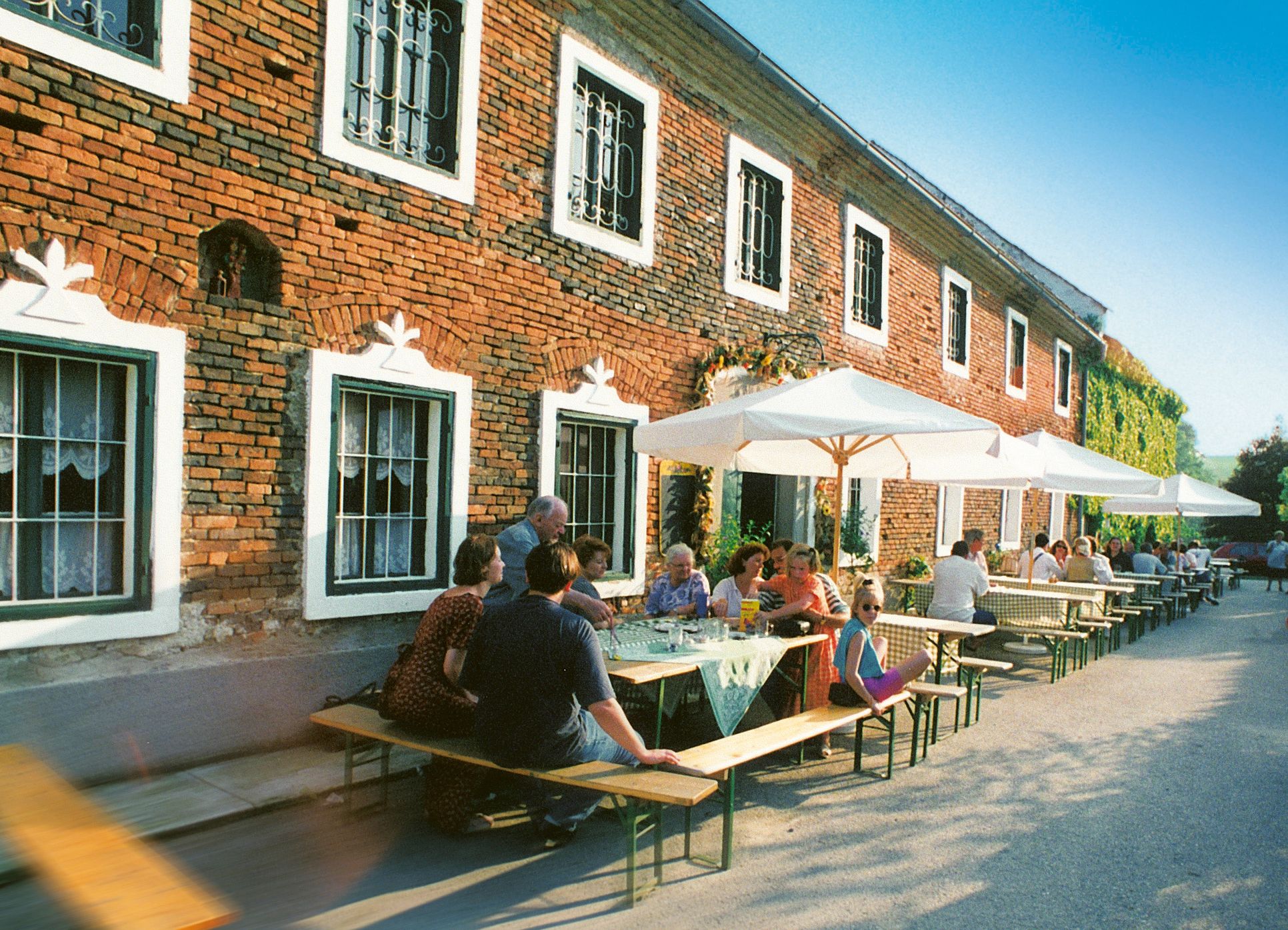 People sit at tables in front of a brick building with parasols.