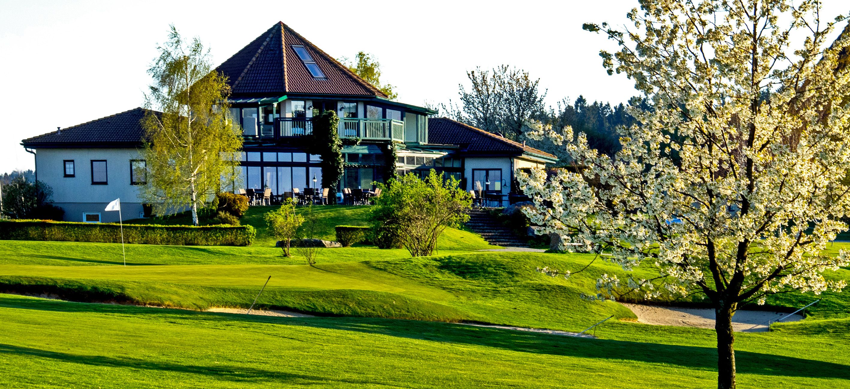Clubhouse of the Ottenstein Golf Club with a blossoming tree in the foreground.