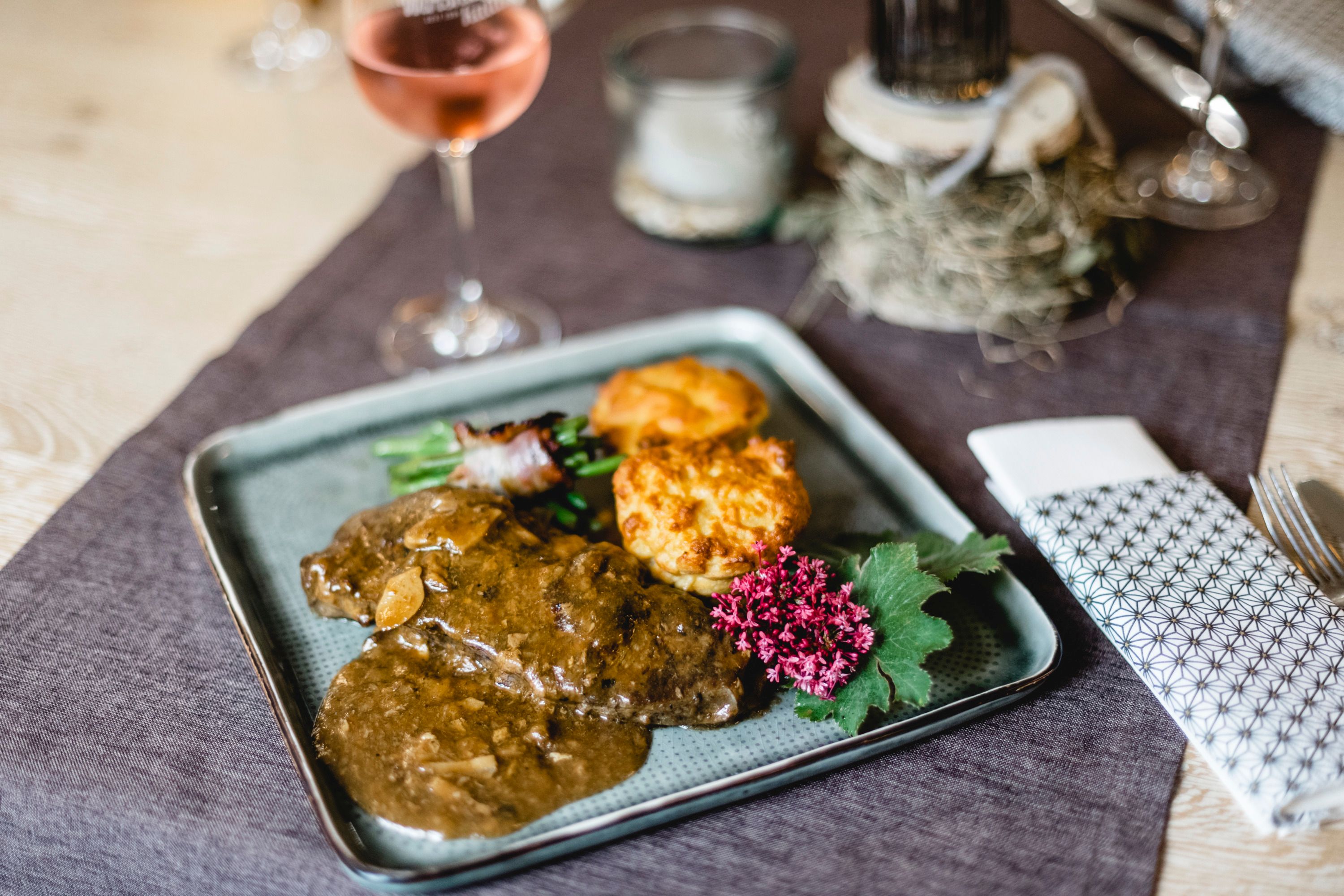 A plate of roast beef stuffed with porcini mushrooms, served with garnishes and a flower as decoration.