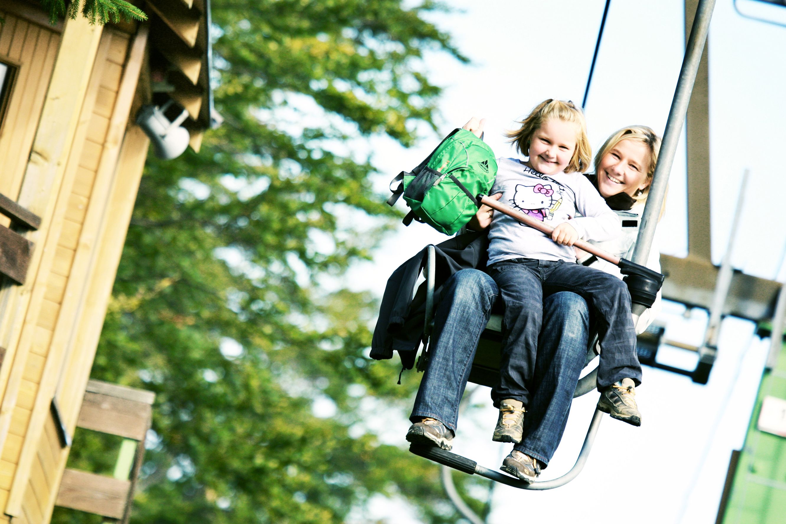 Two people on a chair lift, surrounded by trees.