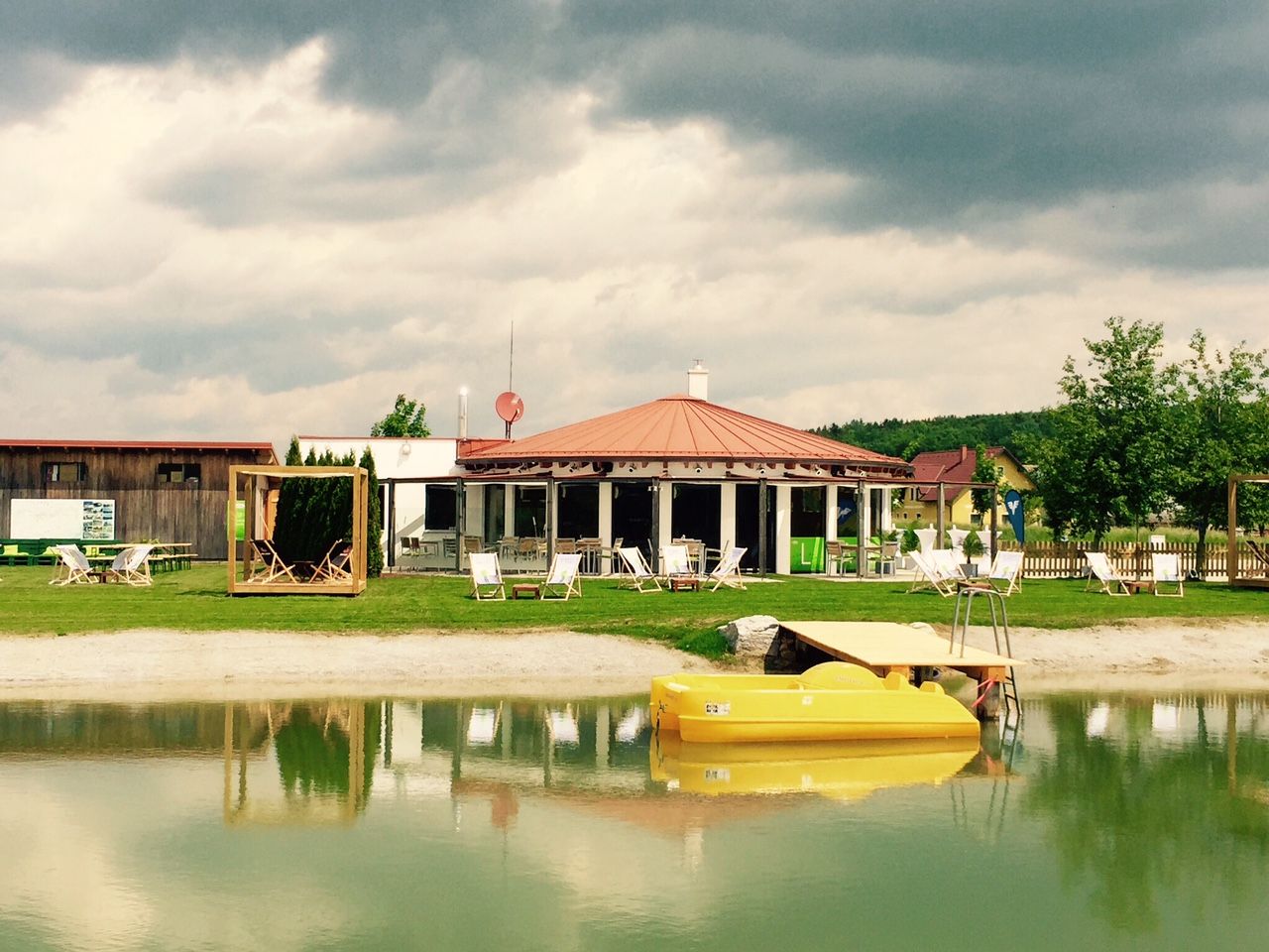 A recreational pond with a yellow pedal boat, deckchairs and a pavilion in the background.