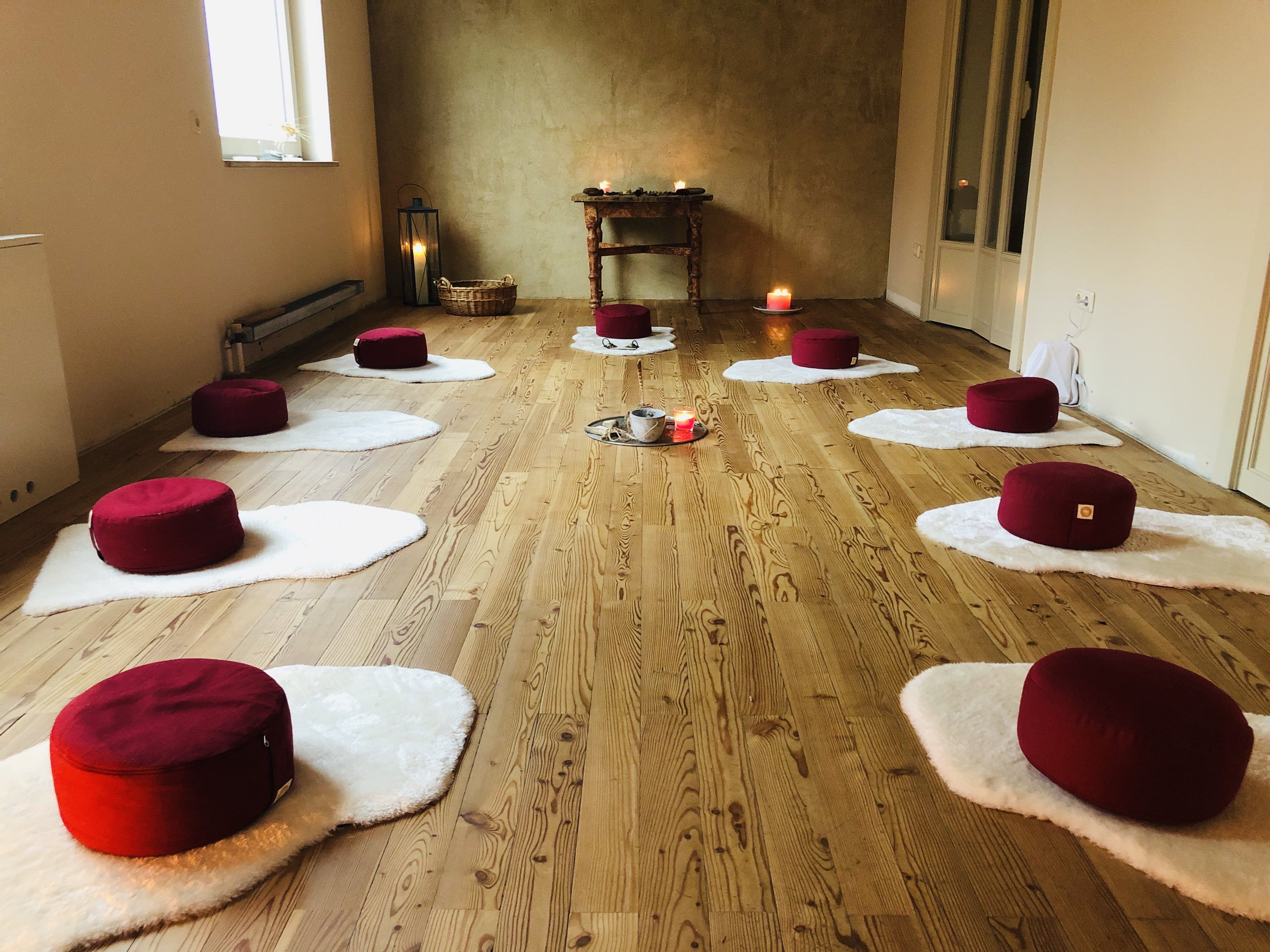Meditation room with red cushions on white mats, candles and wooden floor.