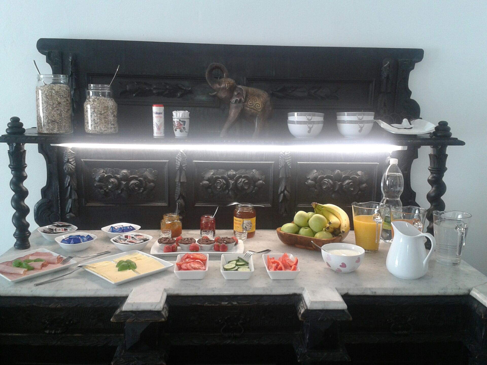 Breakfast buffet with fruit, cold cuts, cheese, jam and drinks on a decorative table.