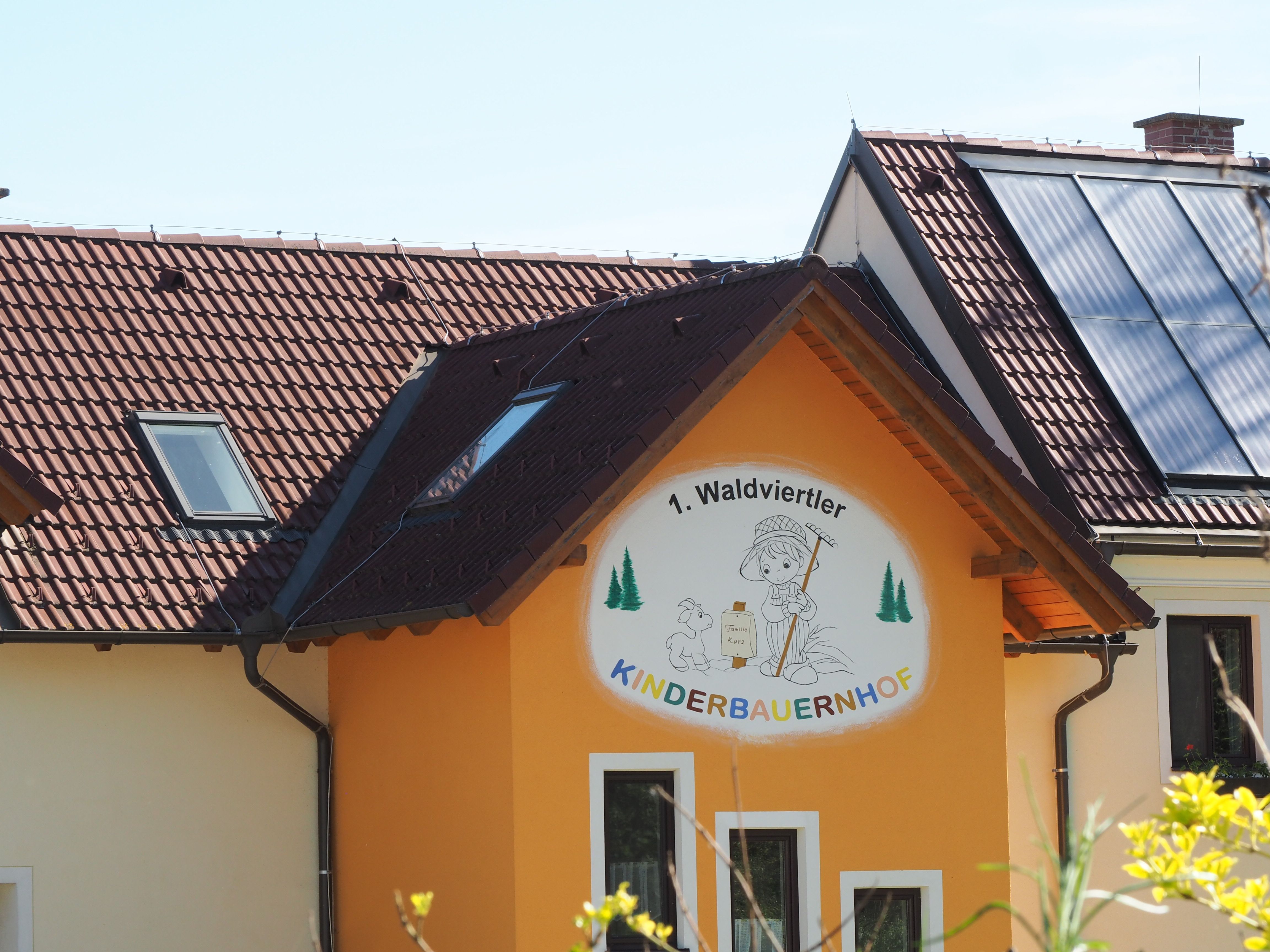 Building with sign '1. Waldviertler Kinderbauernhof', solar panels on the roof.