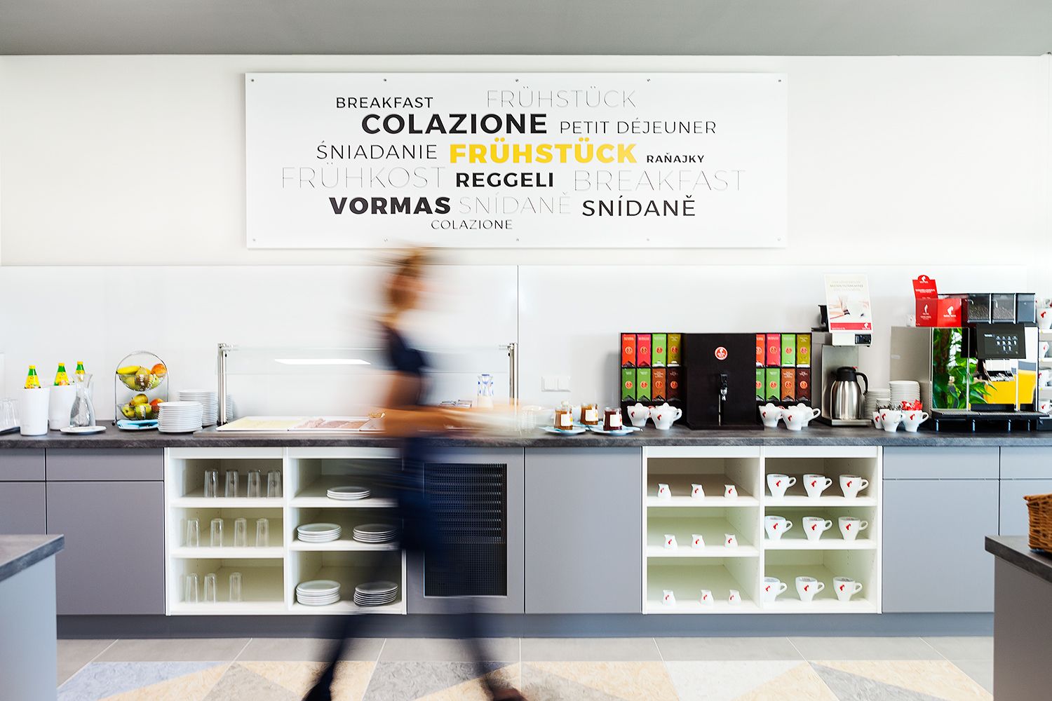 A long gray counter with cups and crockery. Everything for coffee and tea is on the counter.