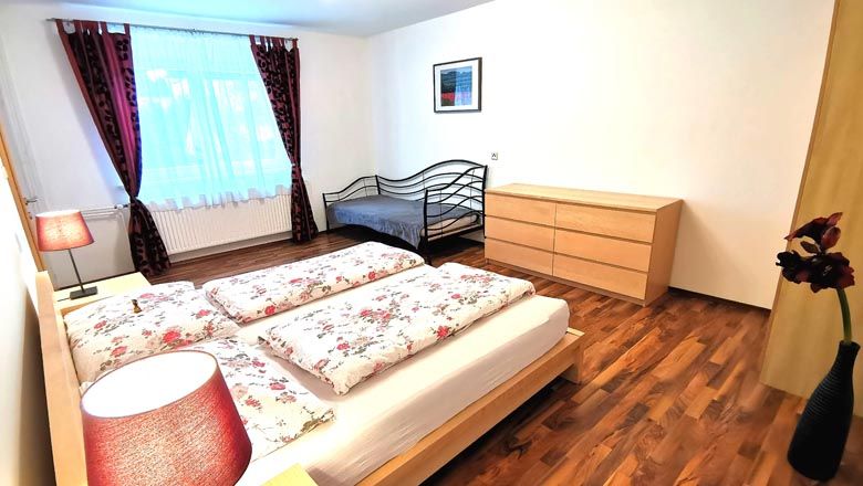 Bedroom with double bed, single bed, chest of drawers and flowers in vase.
