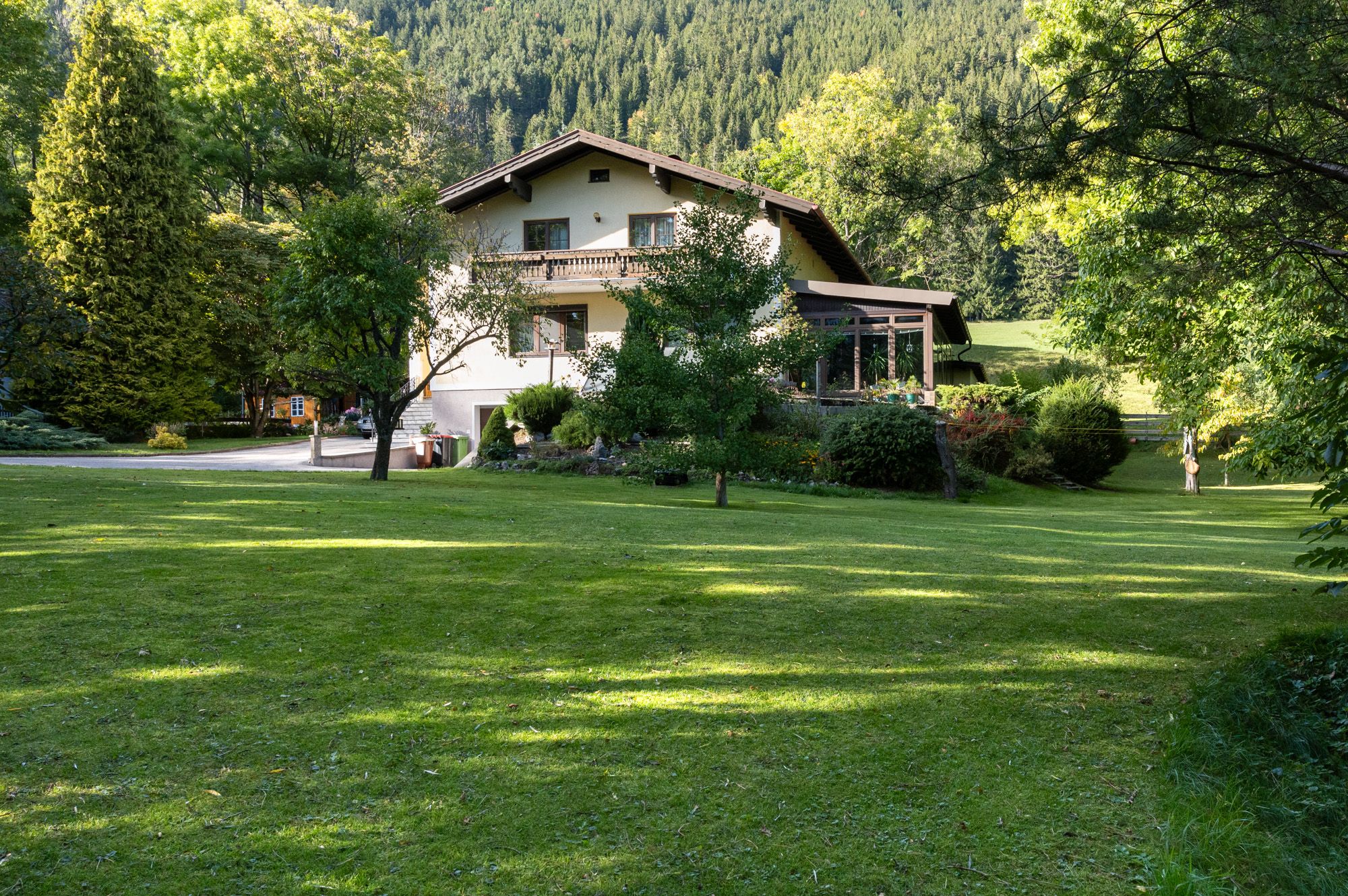 A two-storey vacation home in the middle of a green garden with trees and meadow, surrounded by forest.