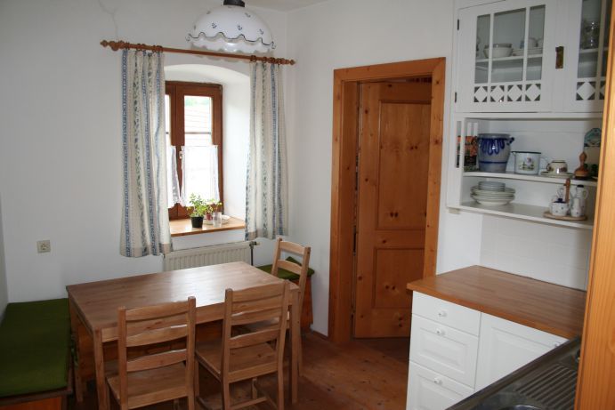 Small kitchen with wooden furniture, dining table, chairs and a window with curtains.