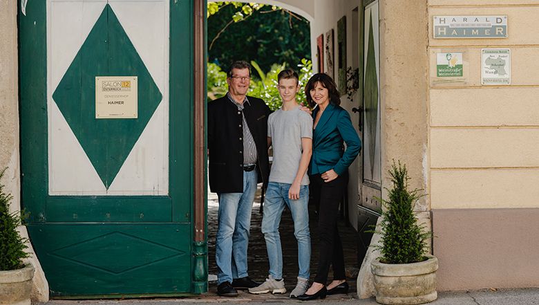 Three people are standing in an archway in front of a building labeled 'Harald Haimer'.