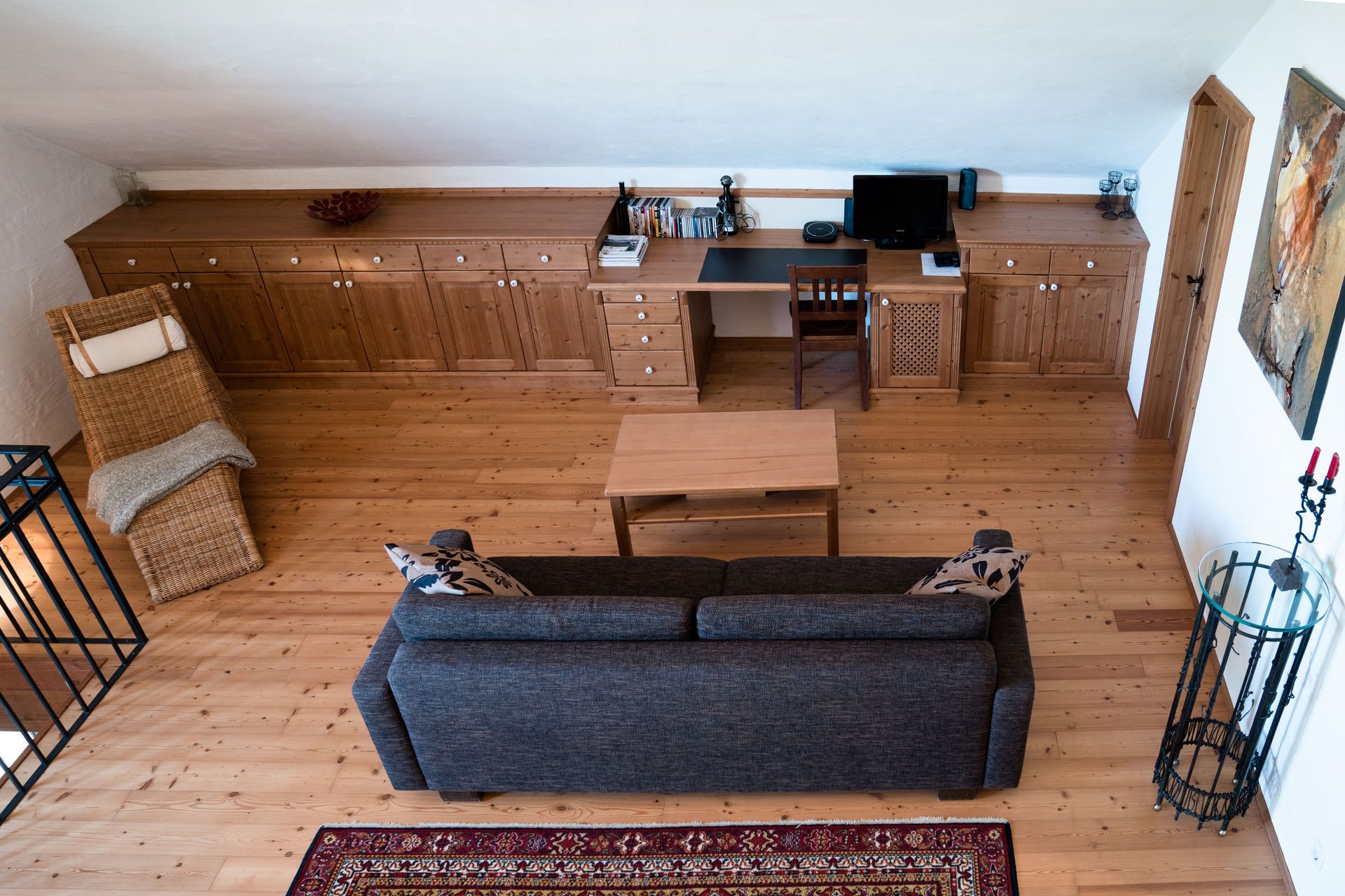 Living room on the upper floor with wooden floor, sofa, table, desk and chair.