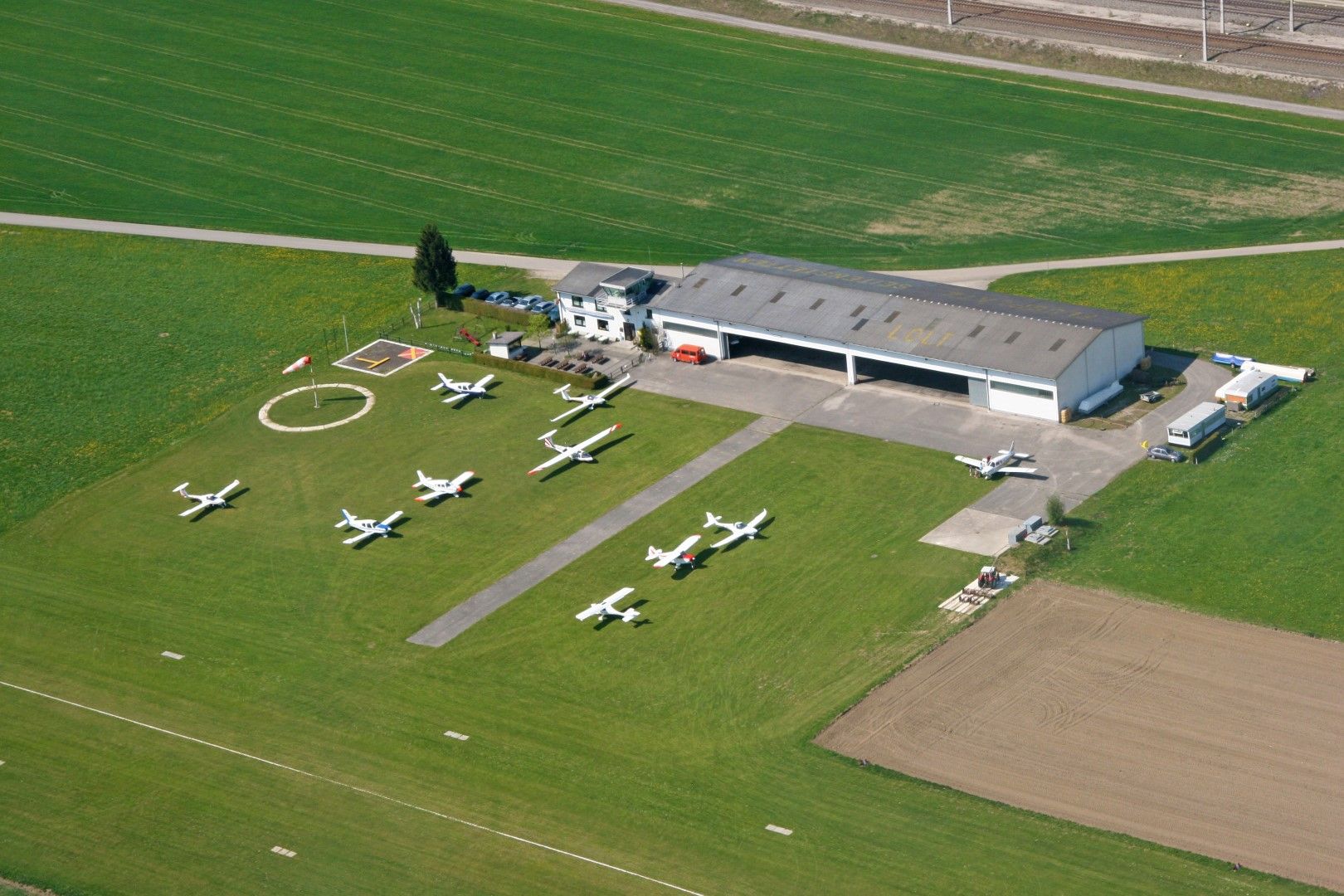Aerial view of a small airfield with several parked airplanes and a hangar.