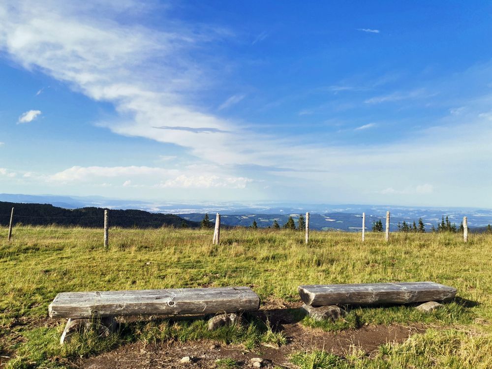 Two wooden benches on a meadow with a wide view over a landscape and blue sky.