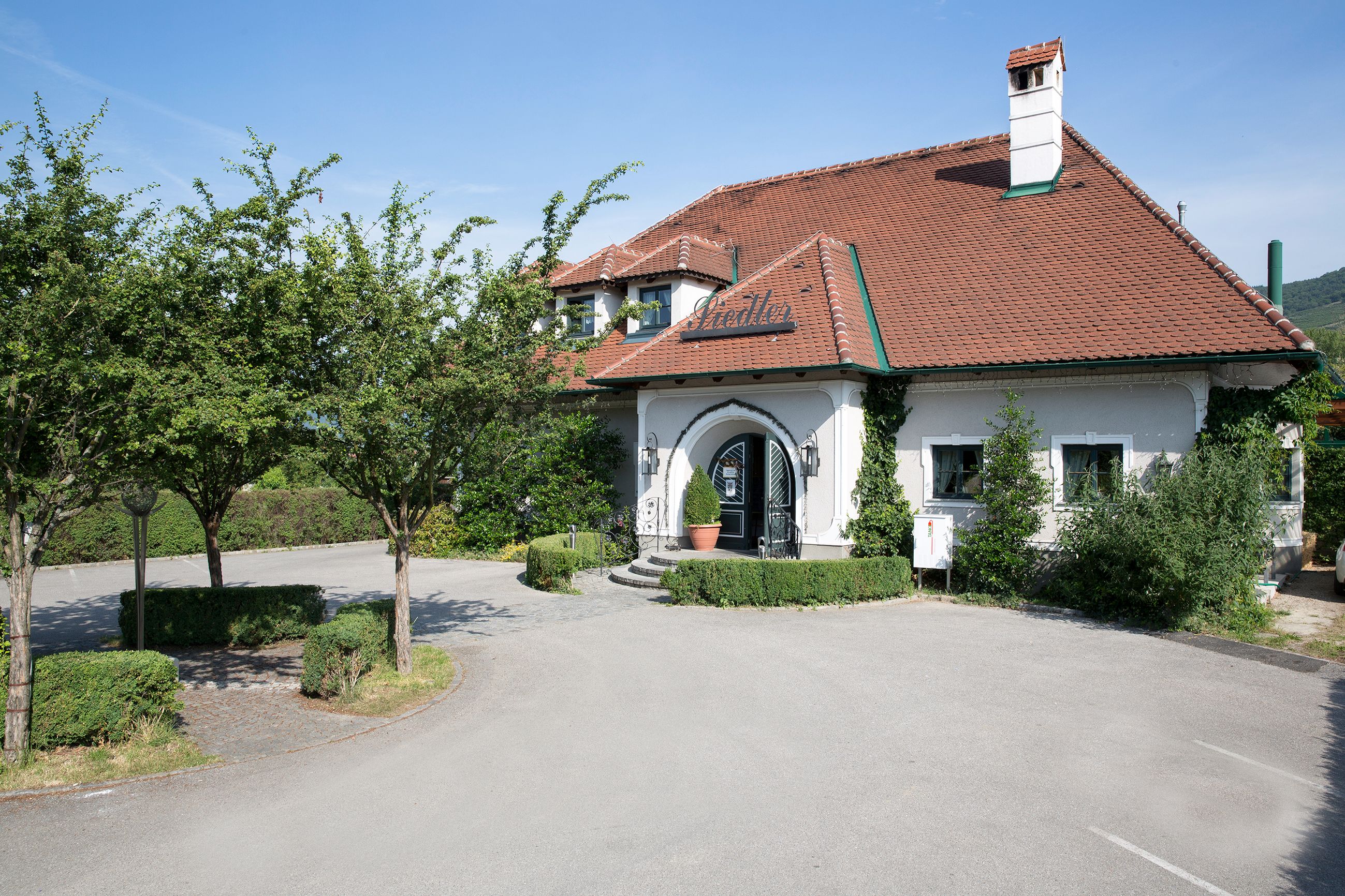 Exterior view of a traditional wine tavern with a red tiled roof and green vegetation.