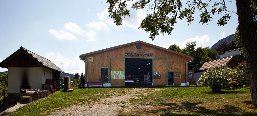 Exterior view of the Maiersdorf village museum with wooden houses and trees.
