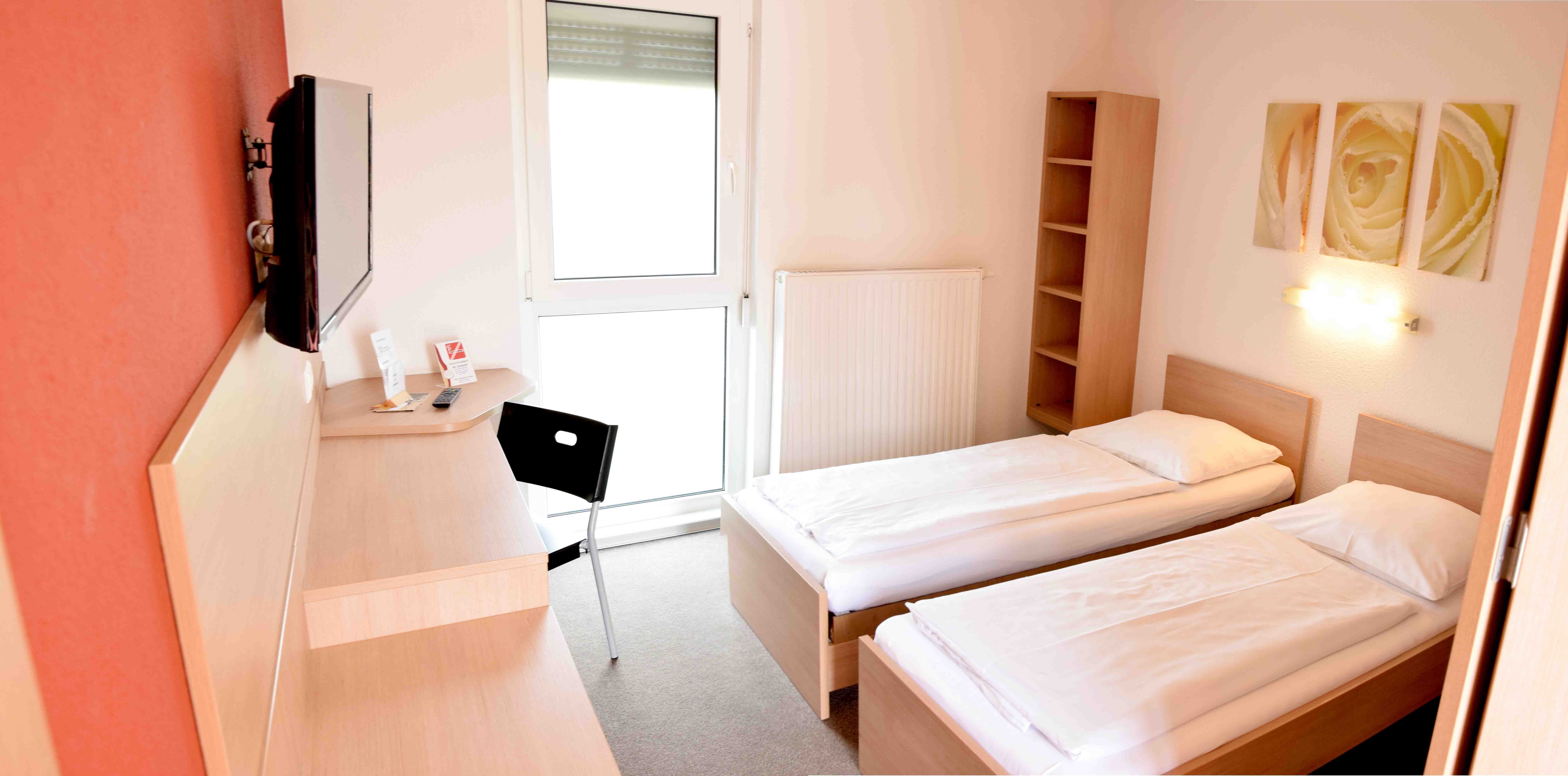 A simple motel room with two single beds, a desk, a chair and a TV on the wall.