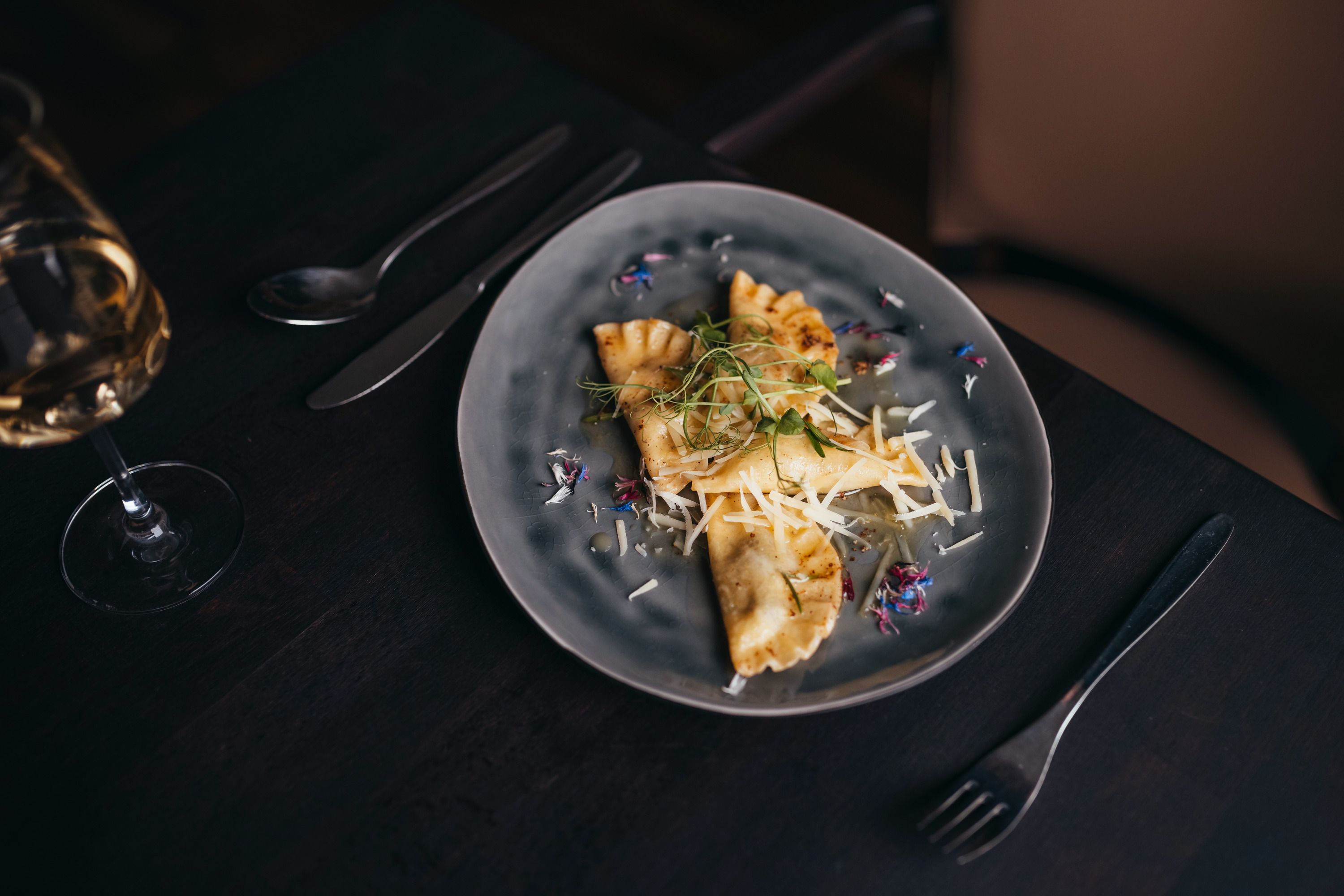 Table set with filled dumplings and grated cheese on a gray plate.
