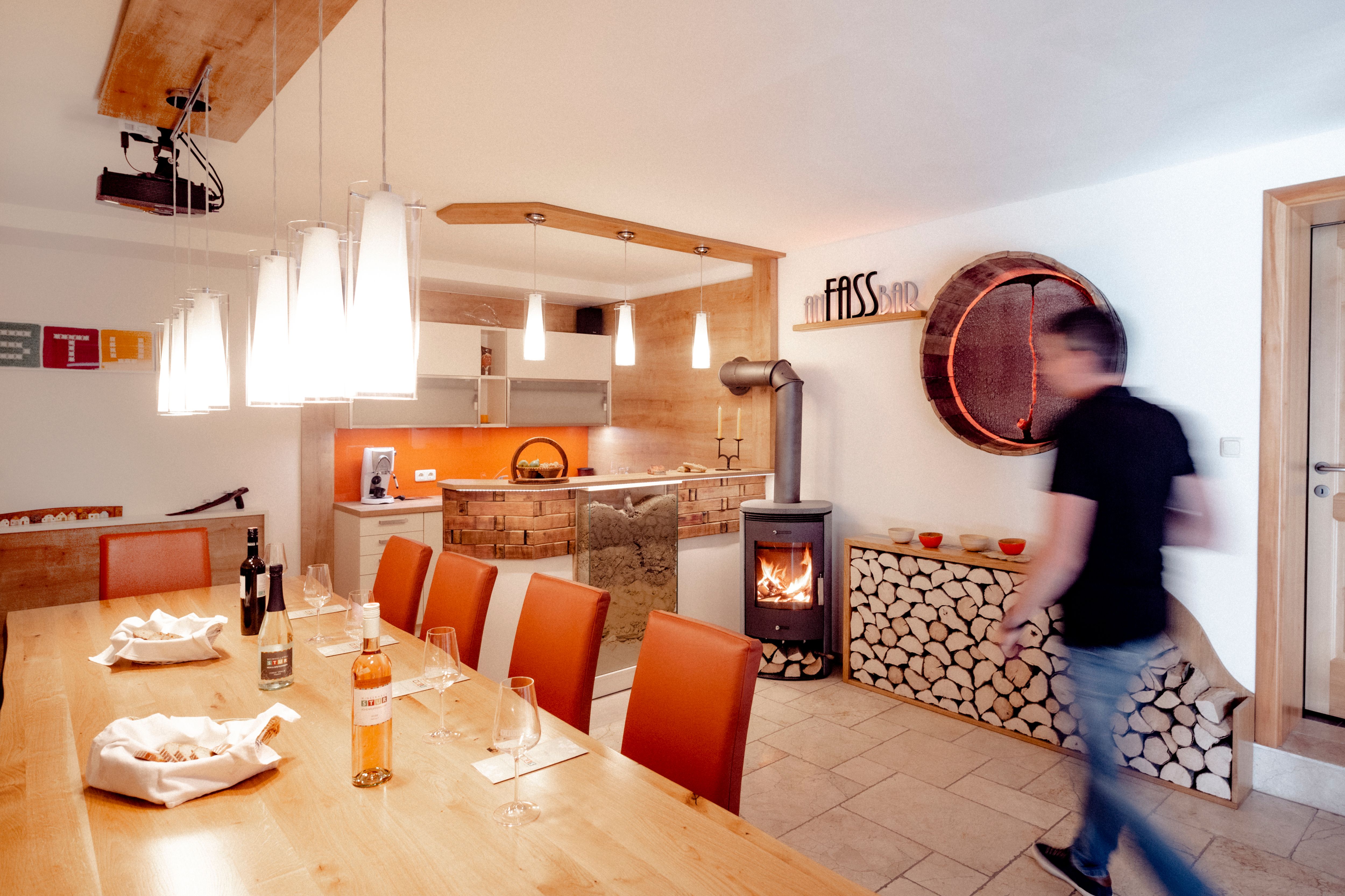 A tasting room with wooden table, wine glasses, fireplace and modern lighting.