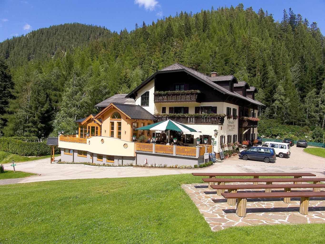 Alpengasthof Kummerbauerstadl in the mountains with terrace and cars.