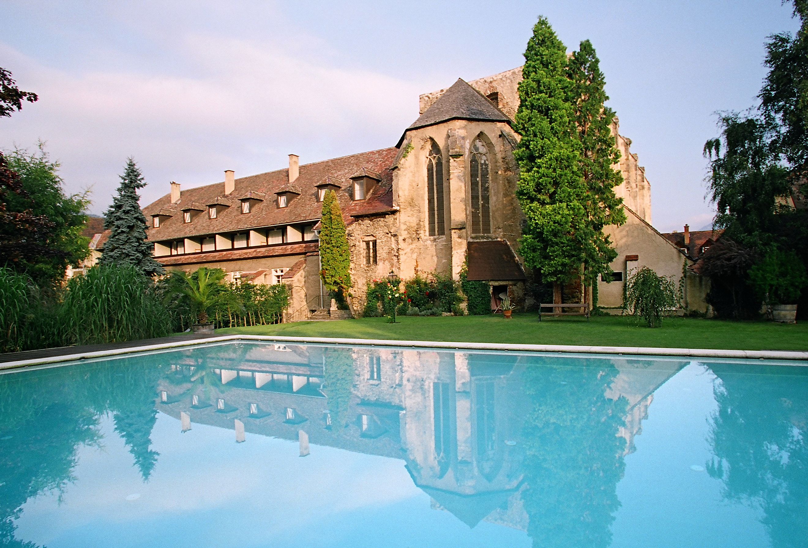 Historic building with pool in the foreground, surrounded by trees and garden.