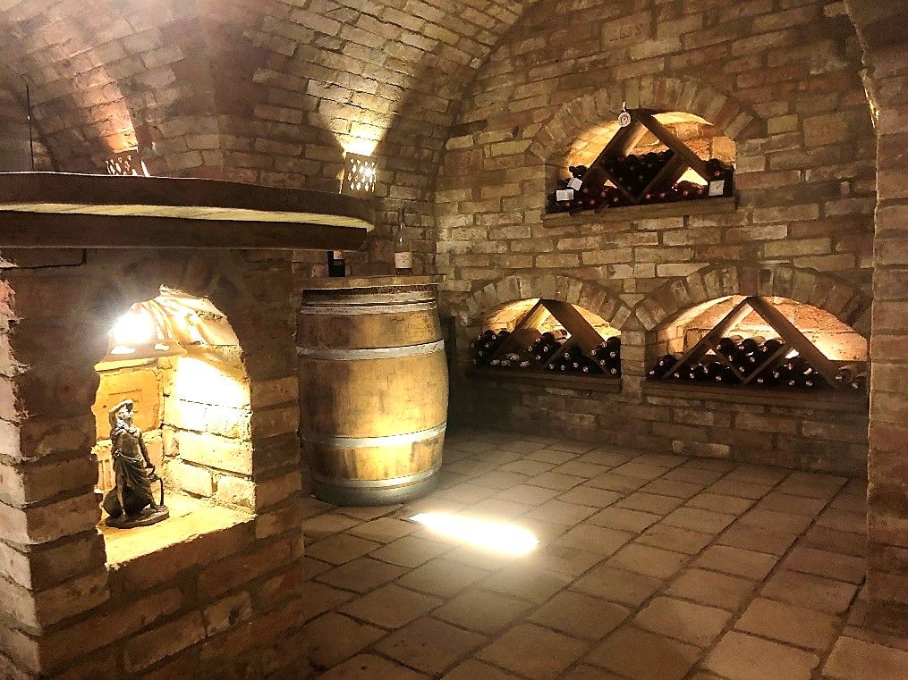 A wine cellar with brick walls, wine racks and a wooden barrel.