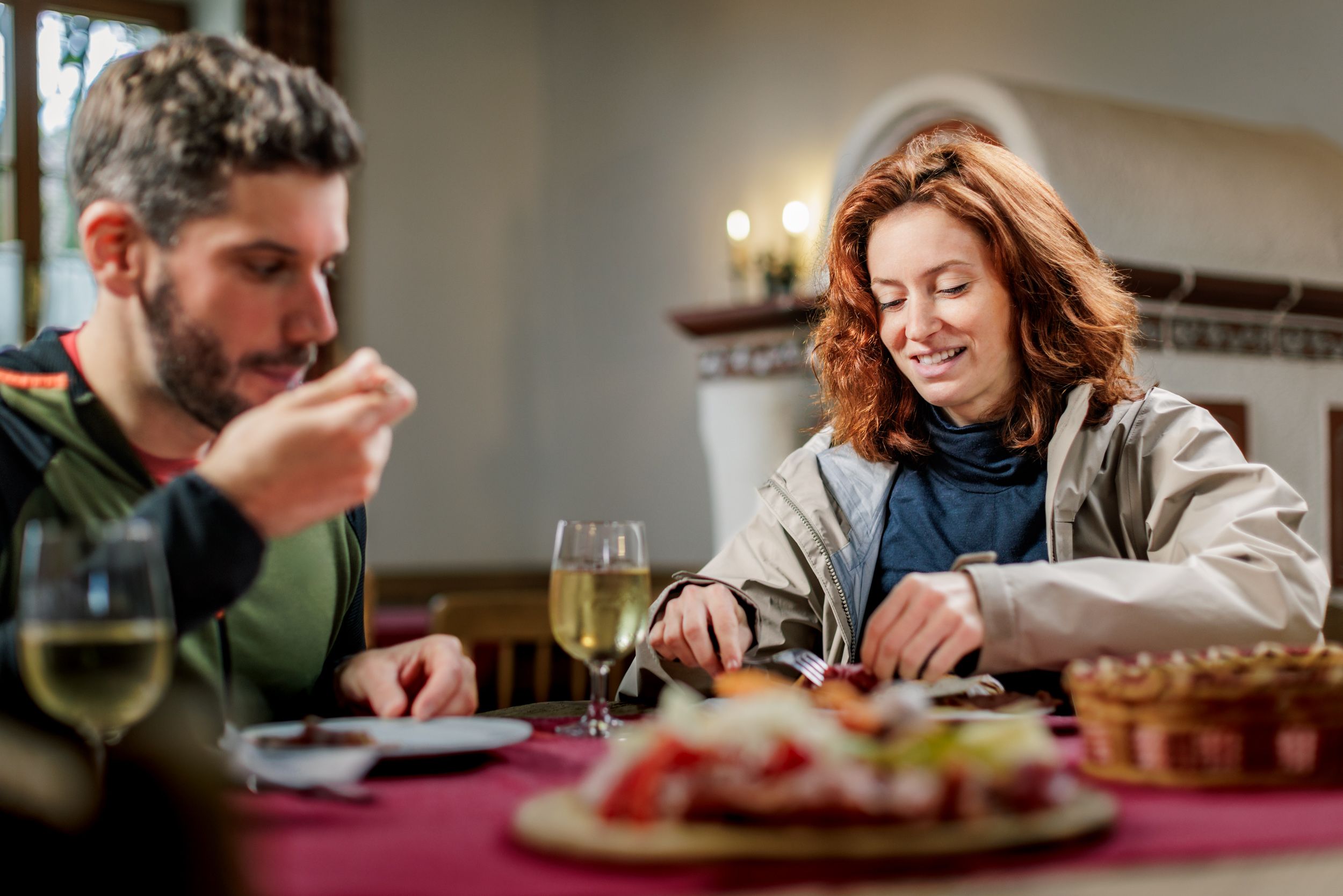 A man and a woman sit in a parlor on a rustic wooden table and eat a Brettljause snack