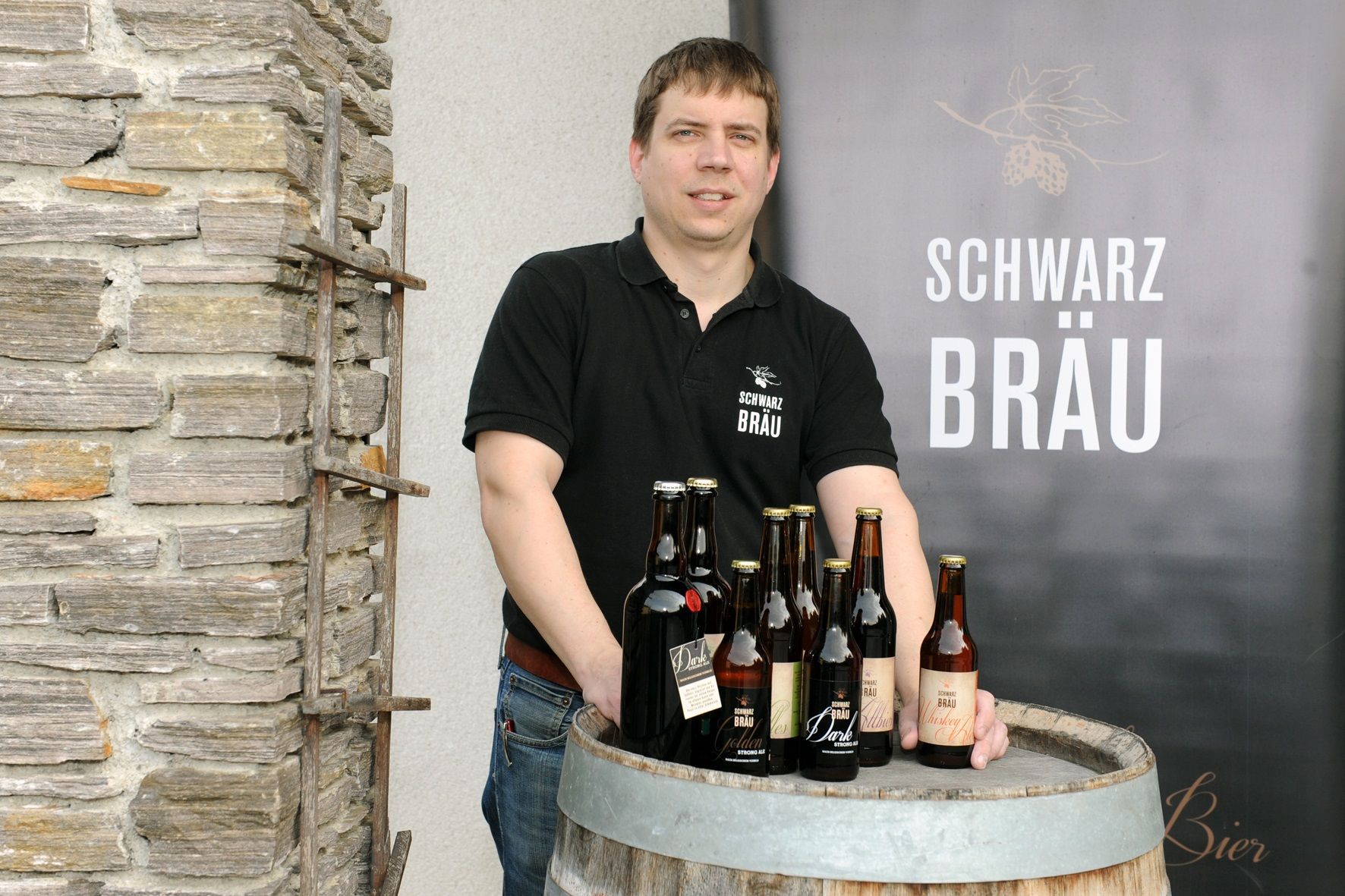 A man stands behind a wooden barrel with bottles of Schwarzbräu beer.
