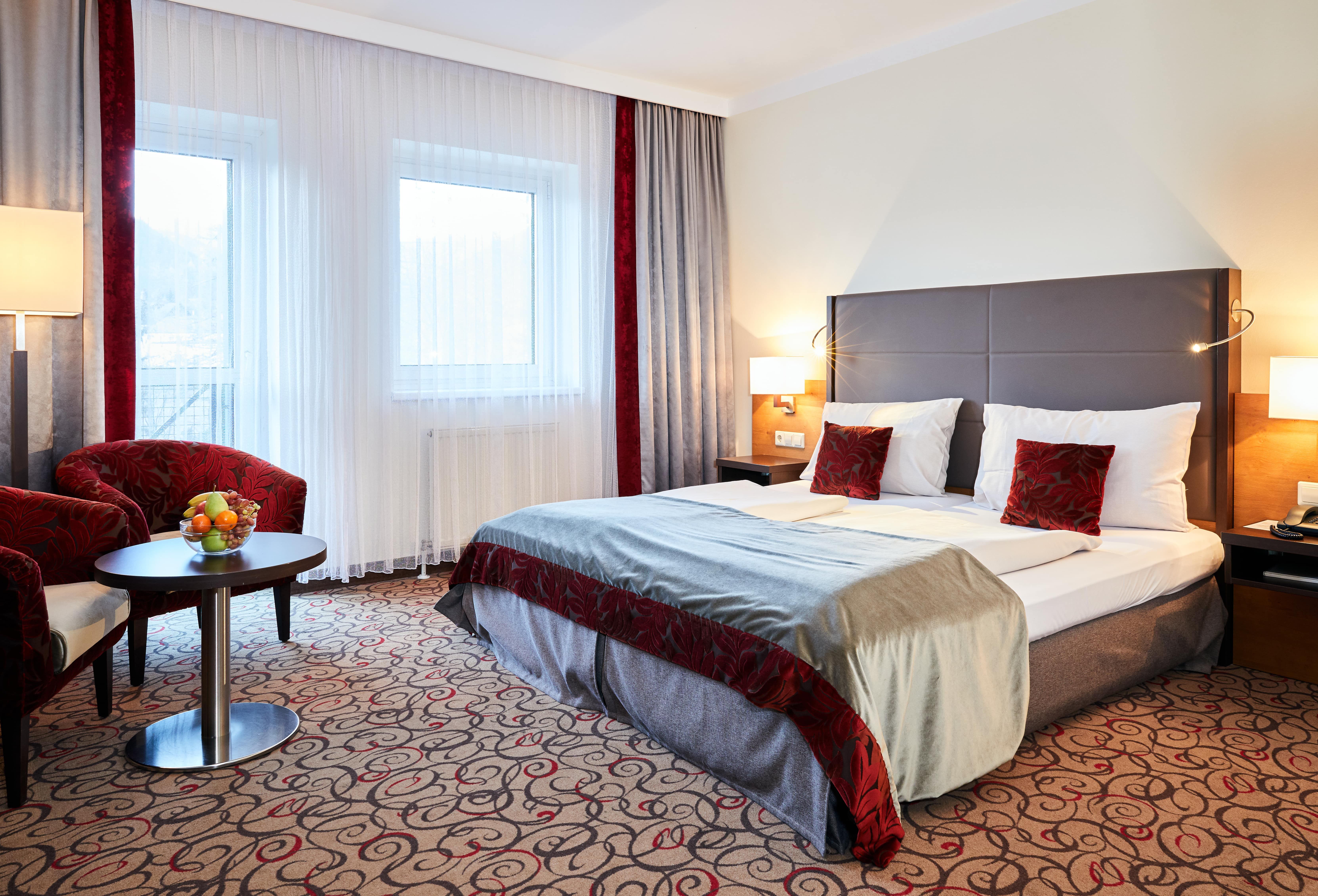 Double room in the Hotel Schneeberghof with double bed, red pillows, table with fruit bowl and two armchairs.