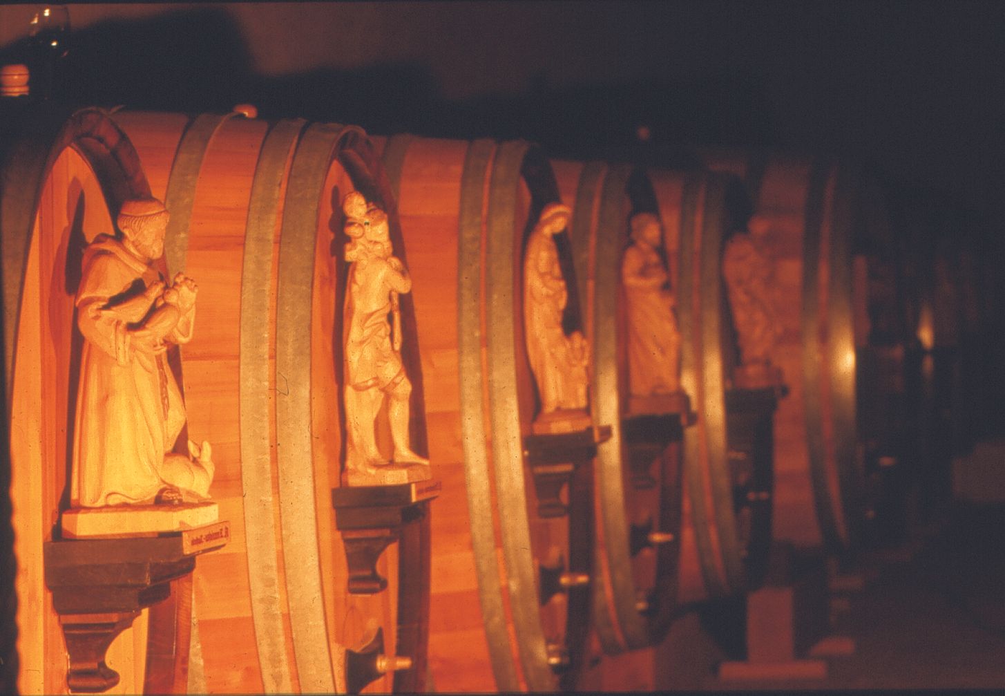 Row of wooden barrels with carved figures in a wine cellar.