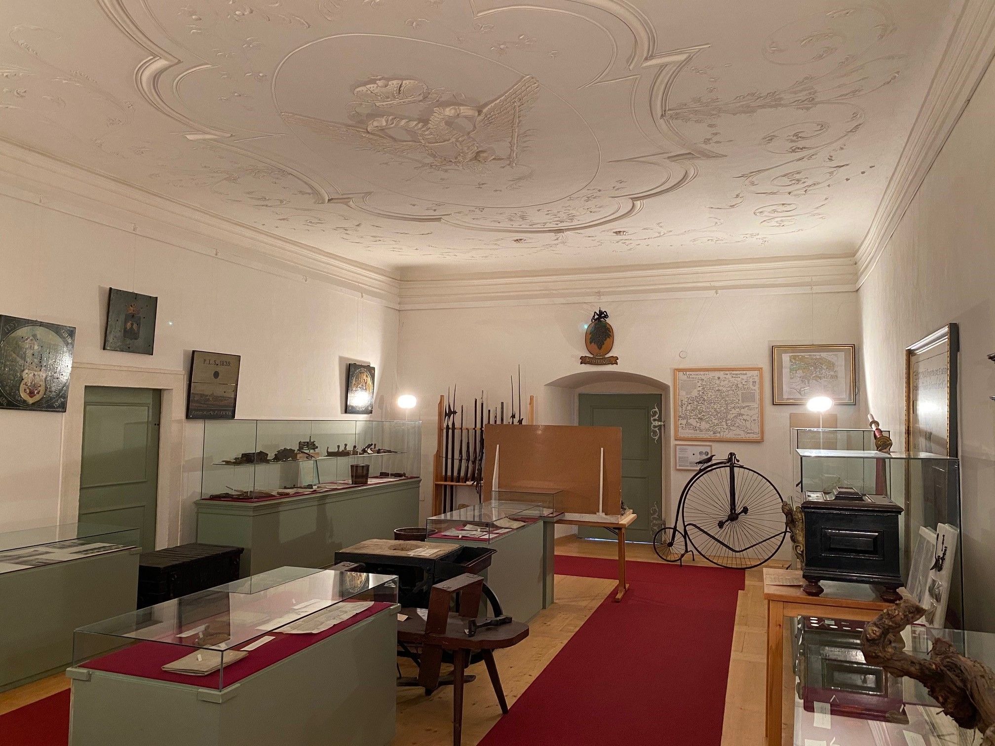 Interior view of a museum room with showcases, old maps and a penny-farthing.
