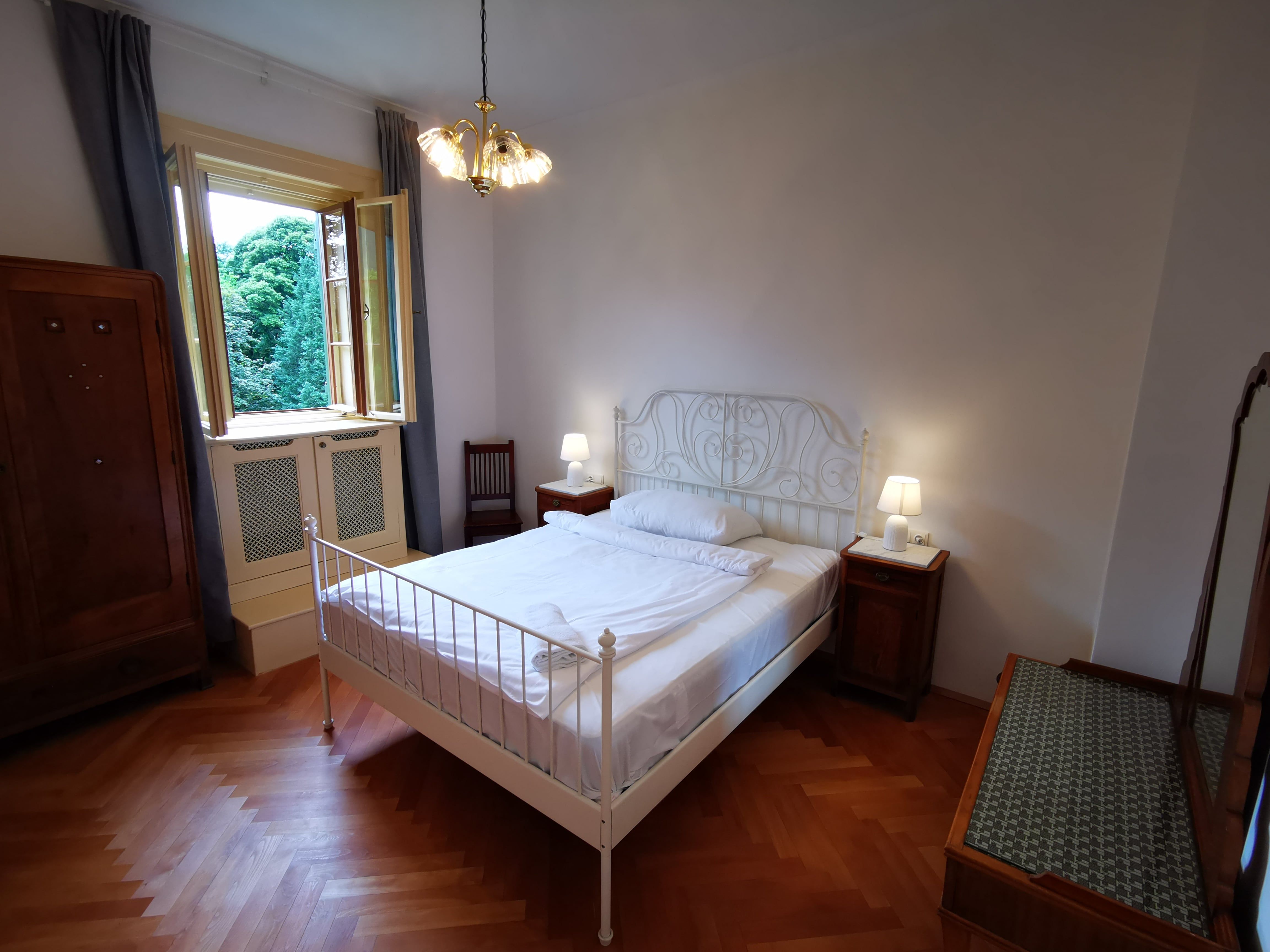 Bedroom with double bed, bedside tables and open window with a view of the trees.
