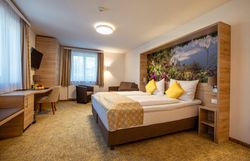 Modern hotel room with double bed, yellow pillows, desk, armchair and large window.