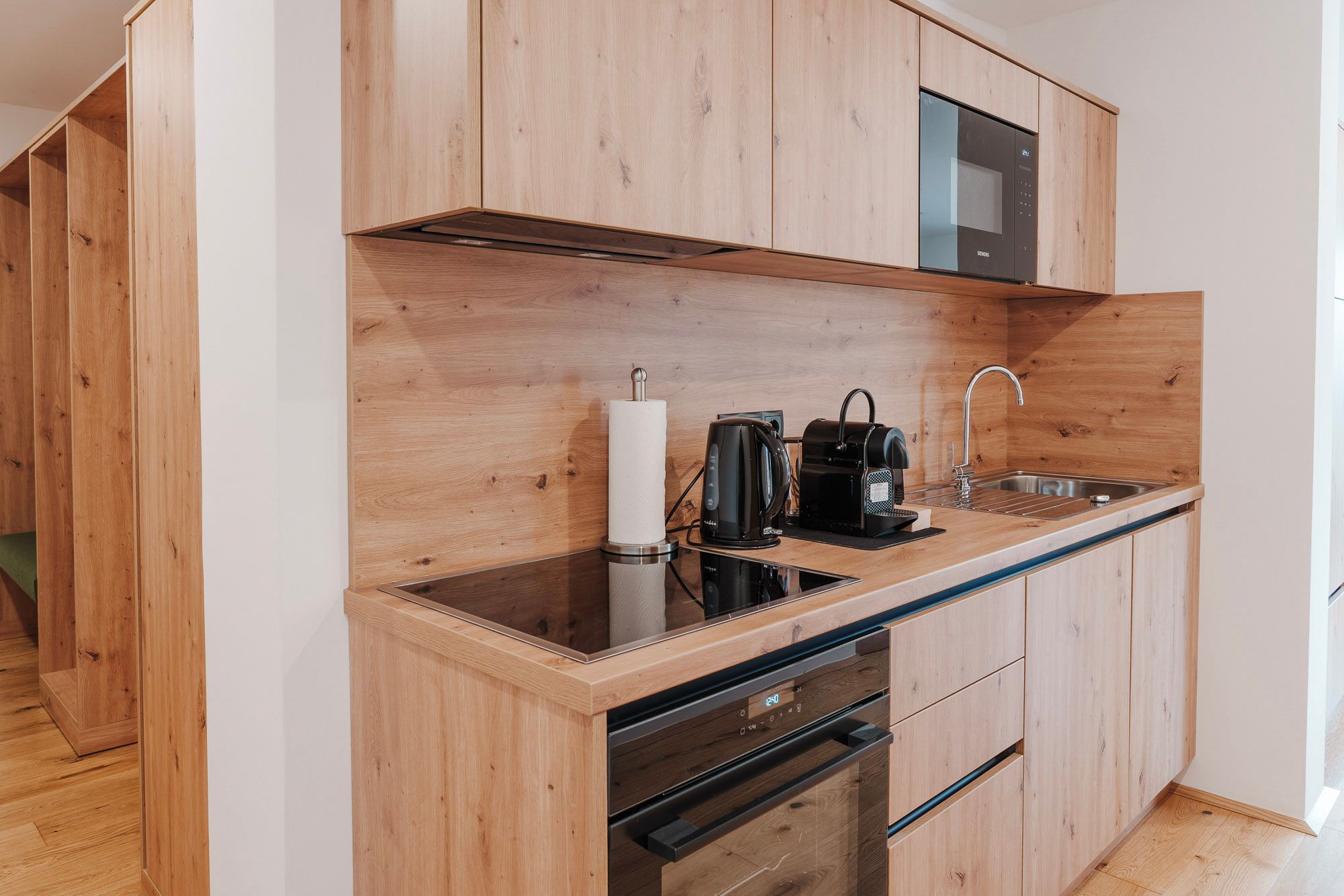 Modern kitchenette with wood paneling, hob, kettle, coffee machine and sink.