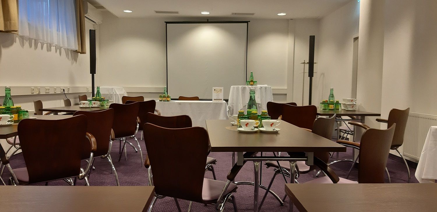 Seminar room with tables, chairs and drinks, projection screen in the background.