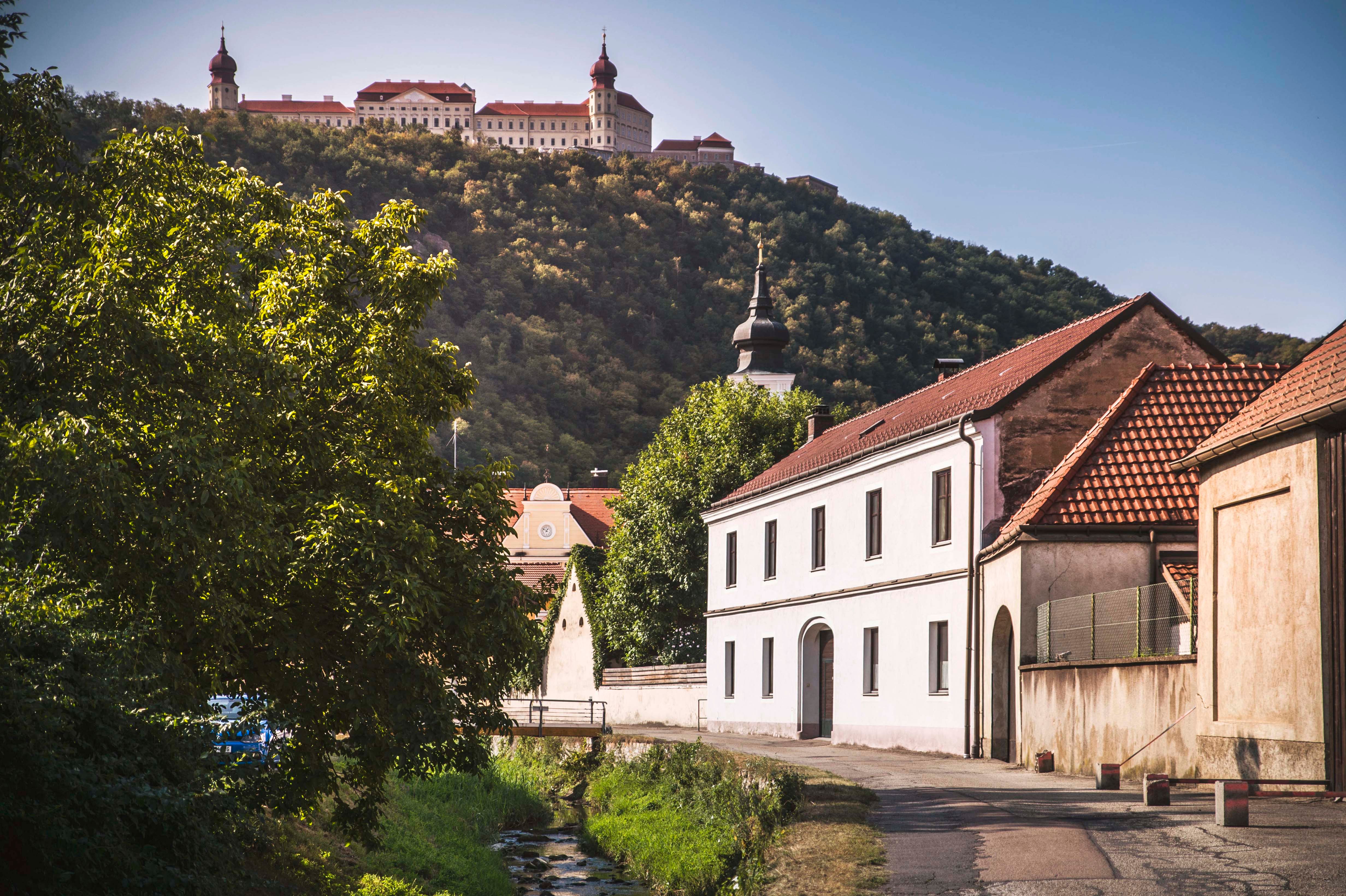 View of Göttweig Abbey on a hill, surrounded by trees, with buildings in the foreground.