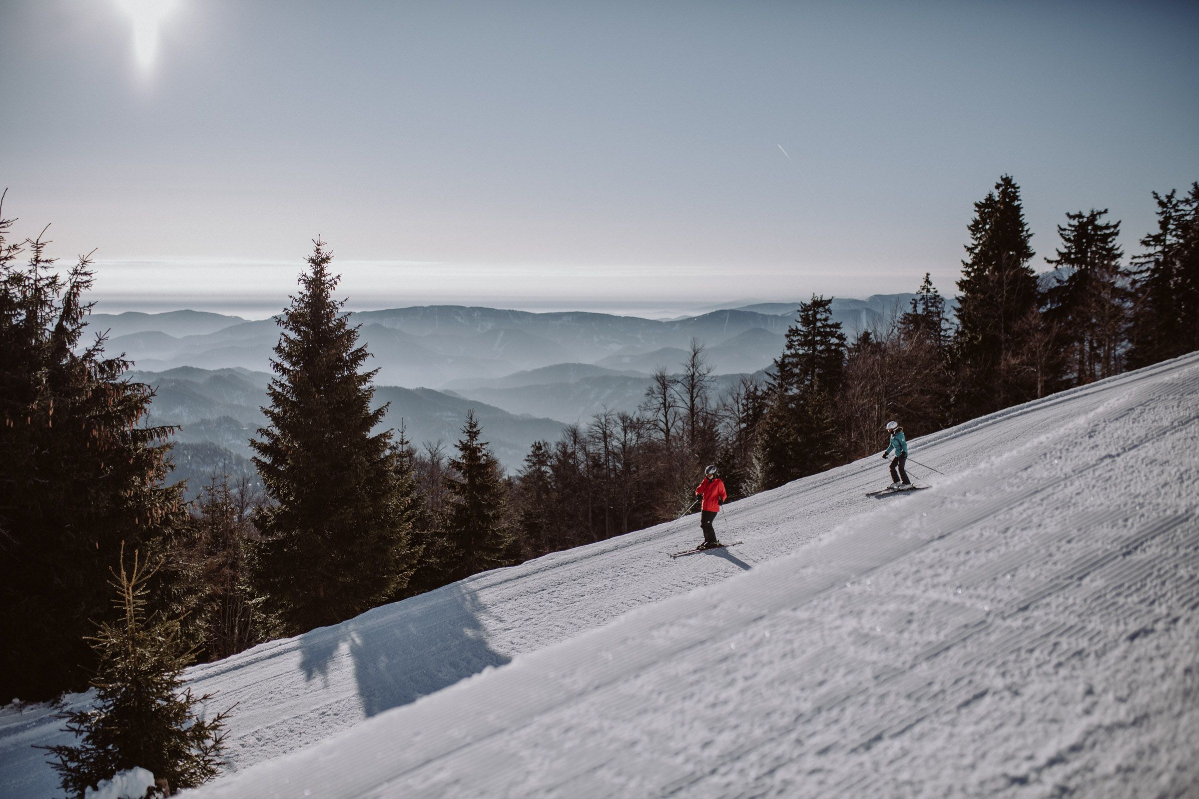 Two skiers on a slope in the Unterberg ski area with a mountain panorama in the background.