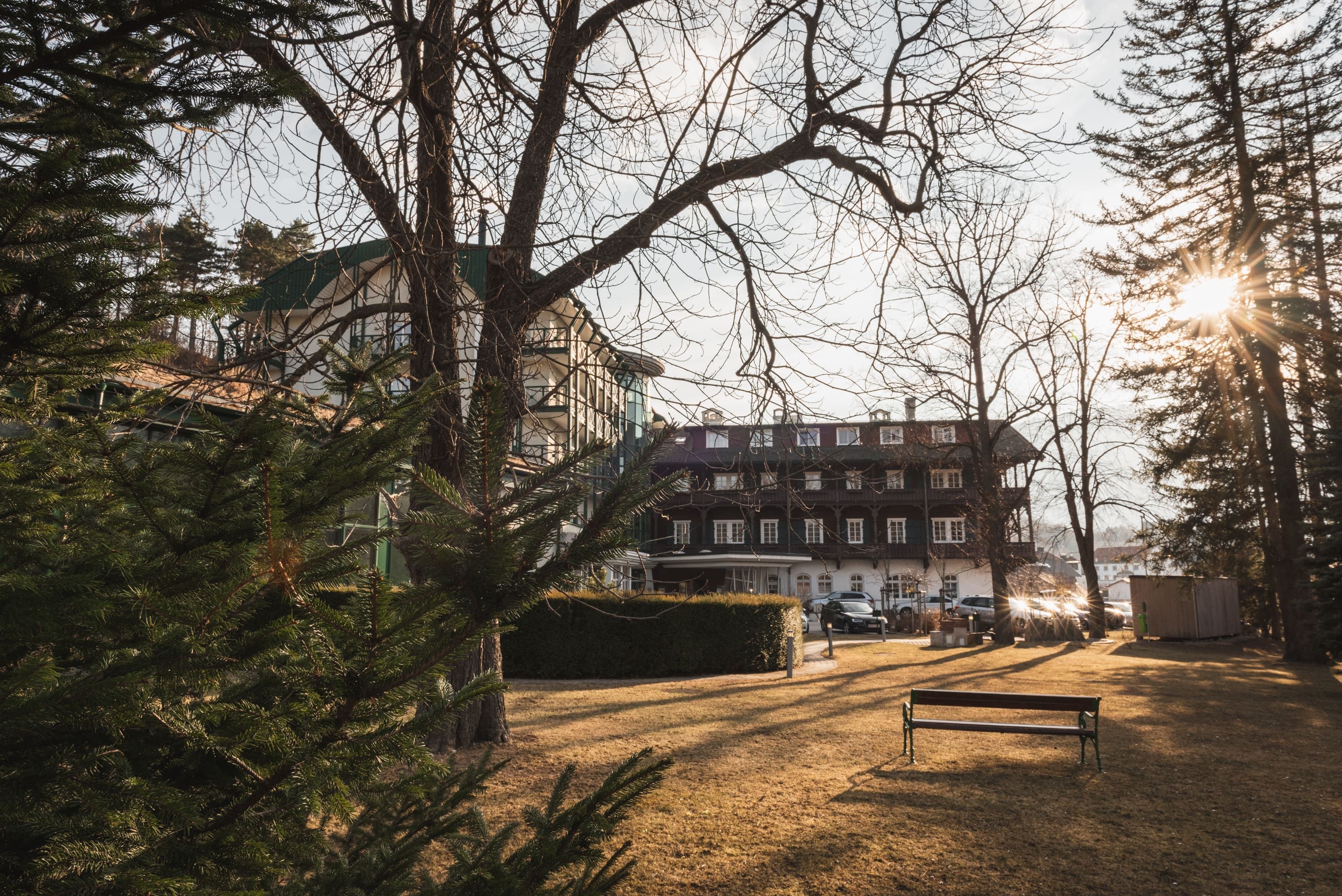Hotel Schneeberghof in the sunlight with trees in the foreground.