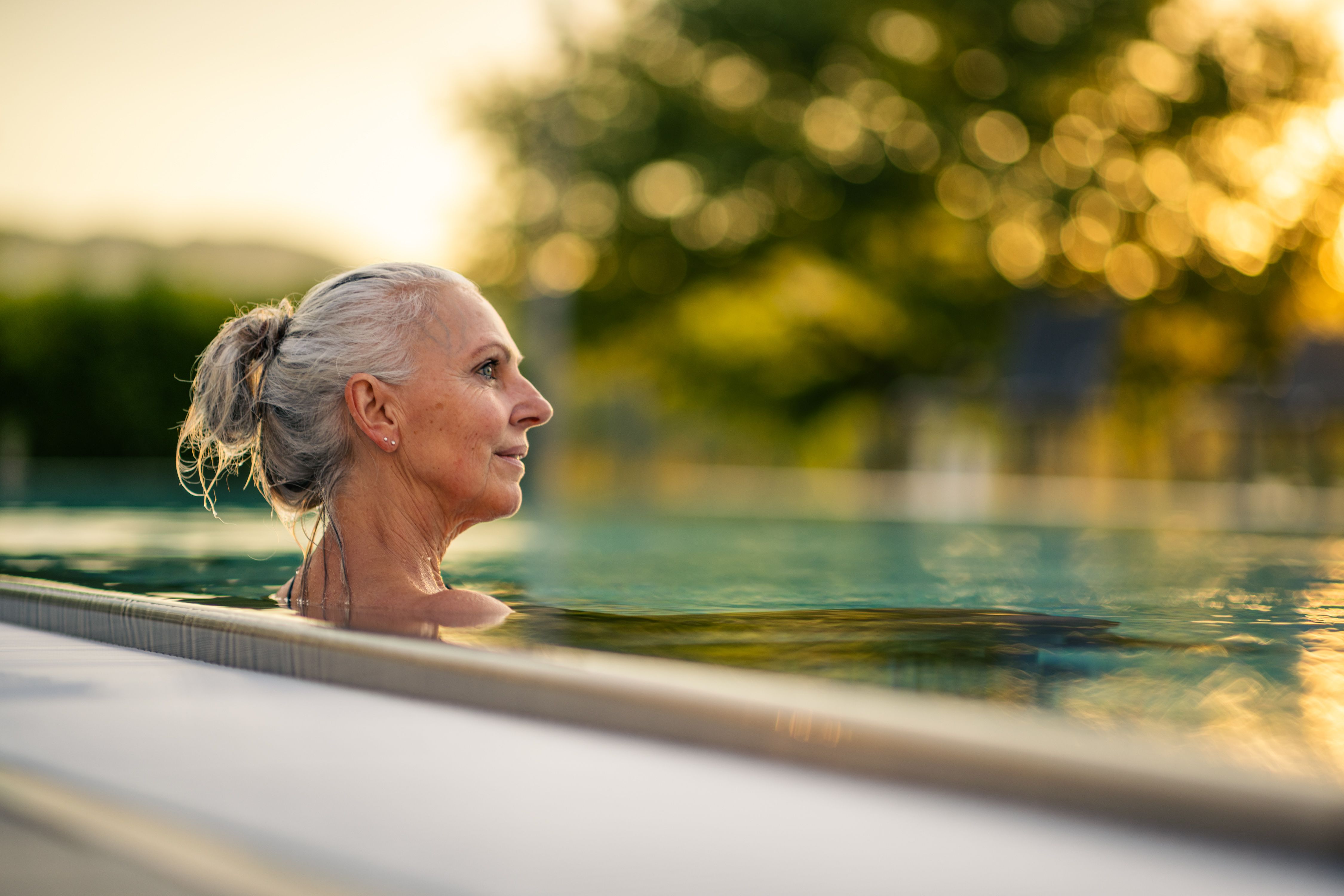 An elderly woman is enjoying a swim in a pool at sunset.