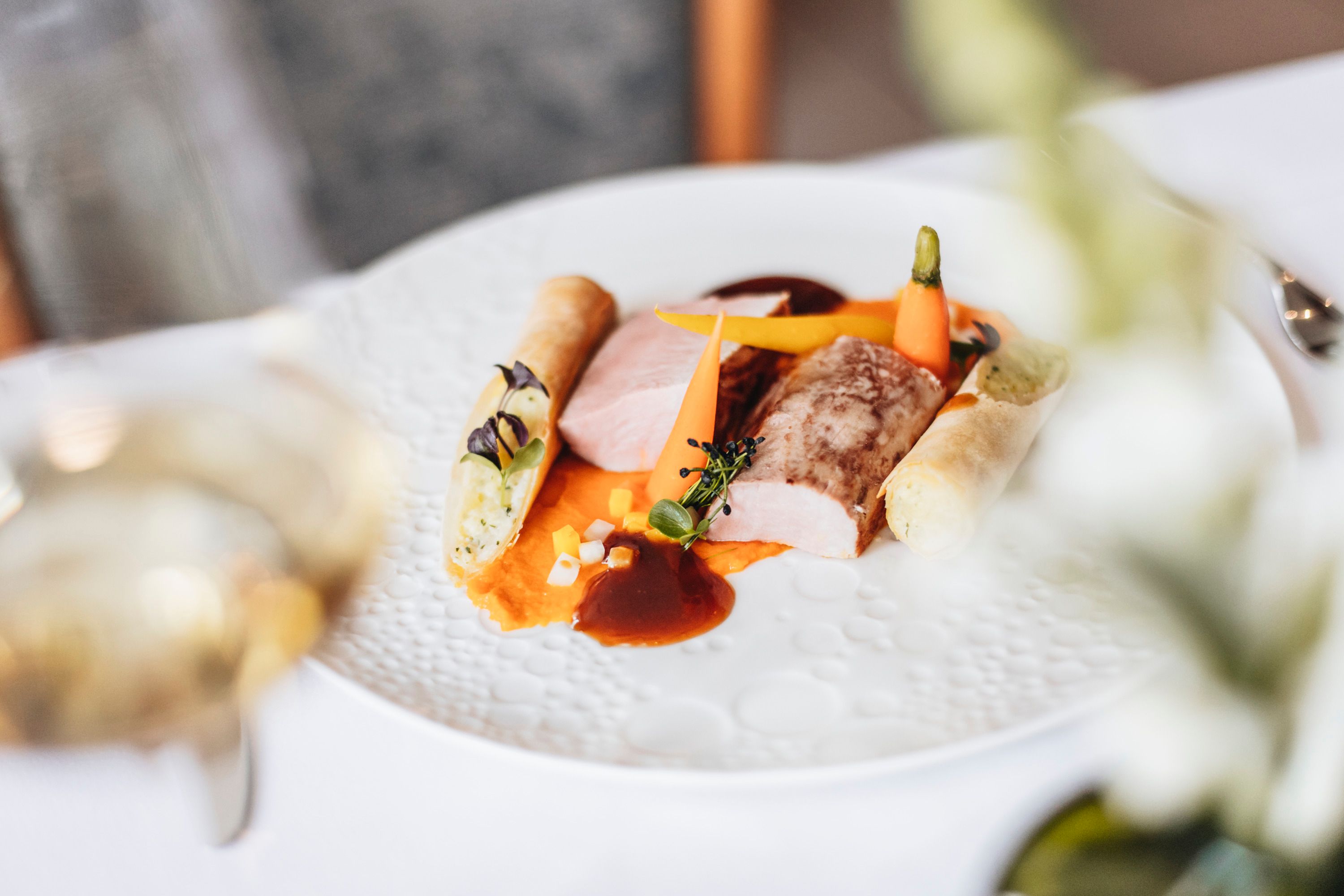 Gourmet dish with pork fillet, vegetables and potato roll on a white plate.