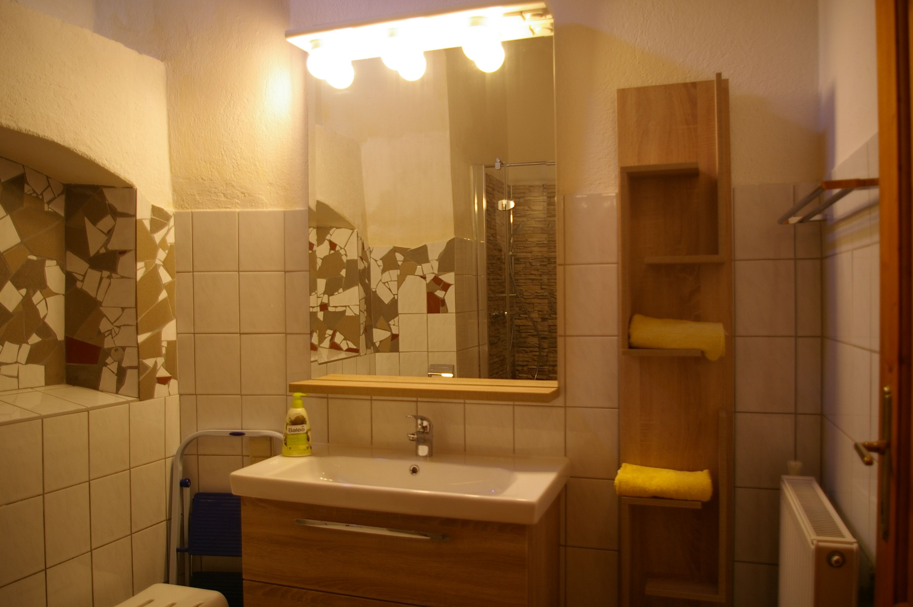 Bathroom with mirror, washbasin, tiles and shelf with towels.