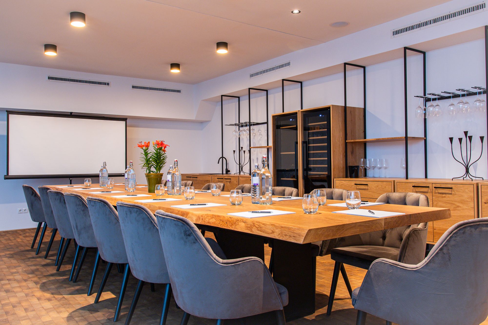 Modern conference room with large wooden table, gray chairs and presentation screen.