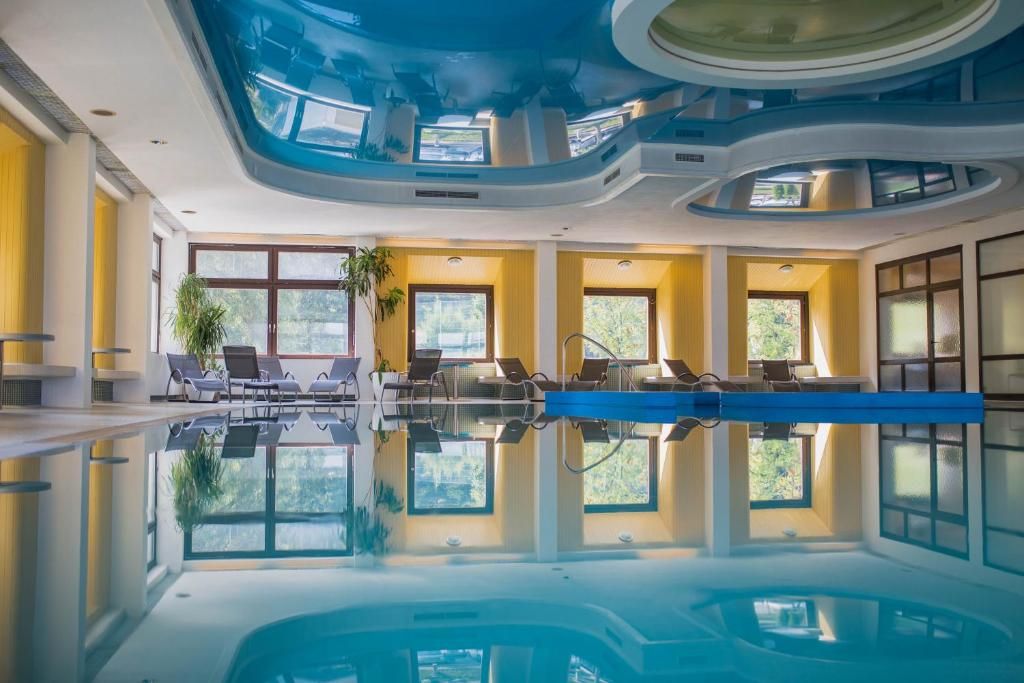 Interior view of an indoor swimming pool with sun loungers and plants at the edge of the pool.