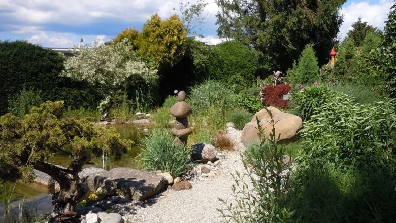 A well-tended garden with a gravel path, stone sculptures and lush vegetation.