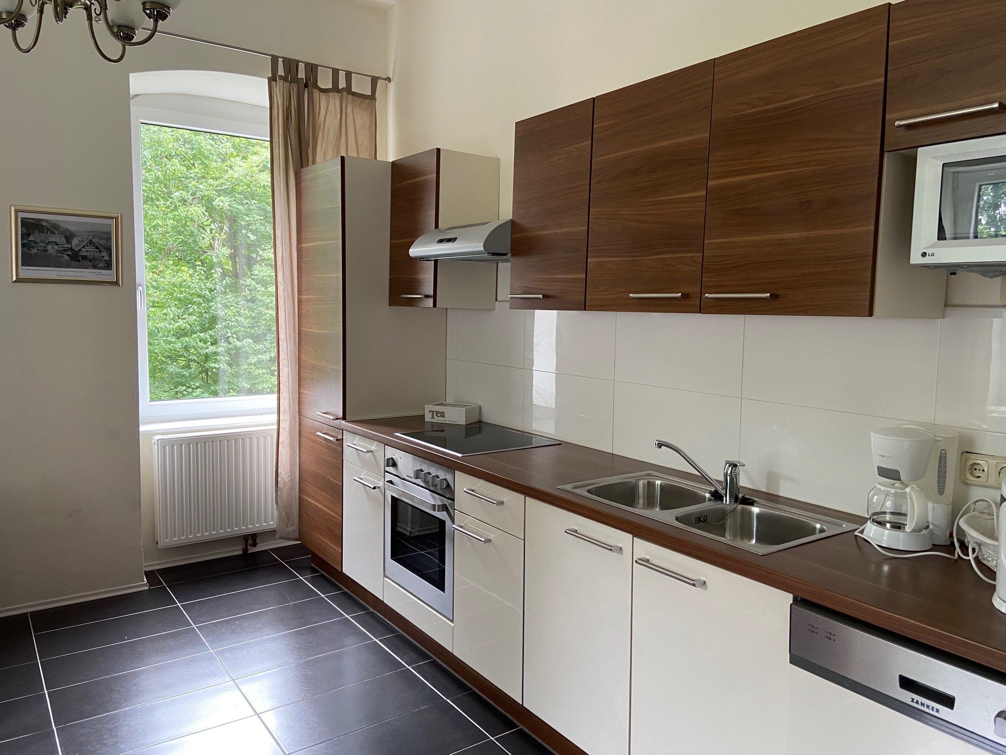 Modern kitchen with wooden cupboards, stove, sink and window with a view of the greenery.