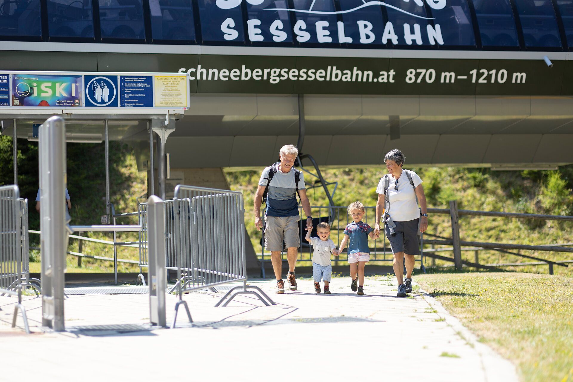A family is enjoying a sunny day in the mountains as they stroll cheerfully toward the chairlift. The children are laughing and holding hands, surrounded by the breathtaking natural beauty of the Schneebergland region. Here, summer in the mountains becomes an unforgettable experience.