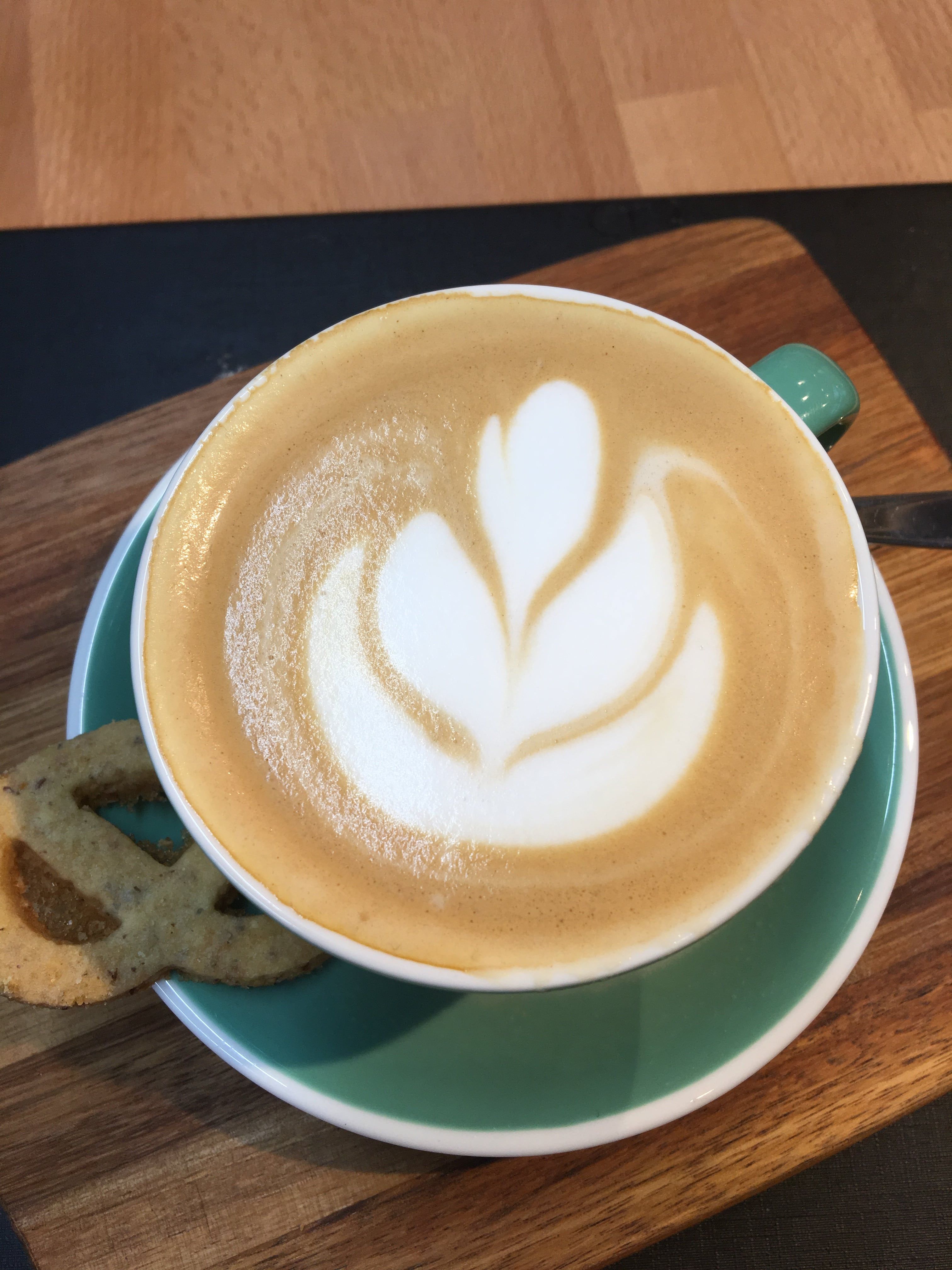 Cappuccino with latte art in a green cup on a wooden board.