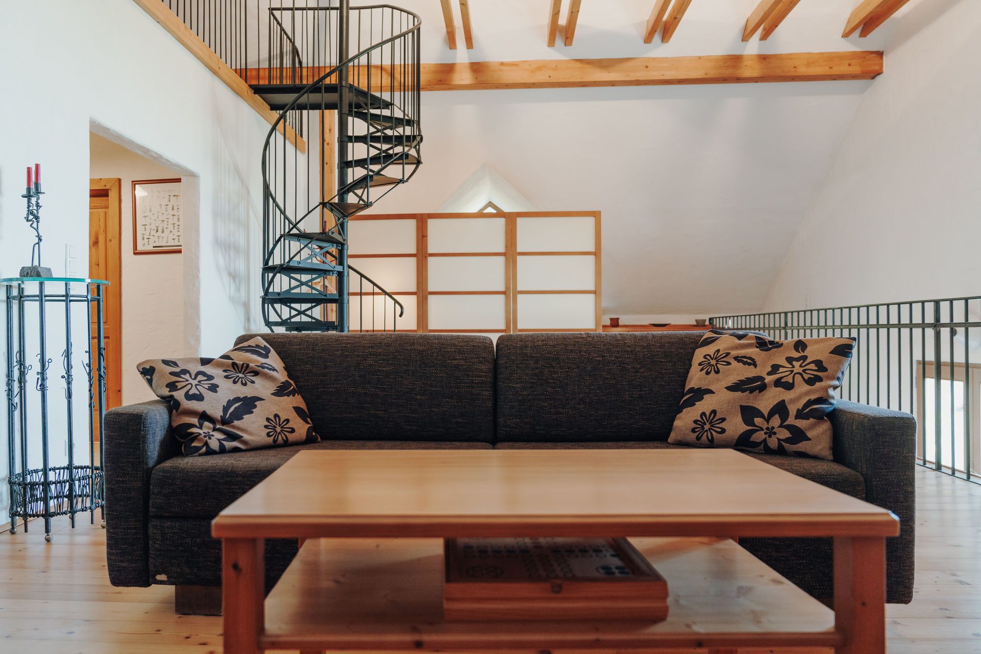 Living room with sofa bed, wooden table and spiral staircase in a loft.