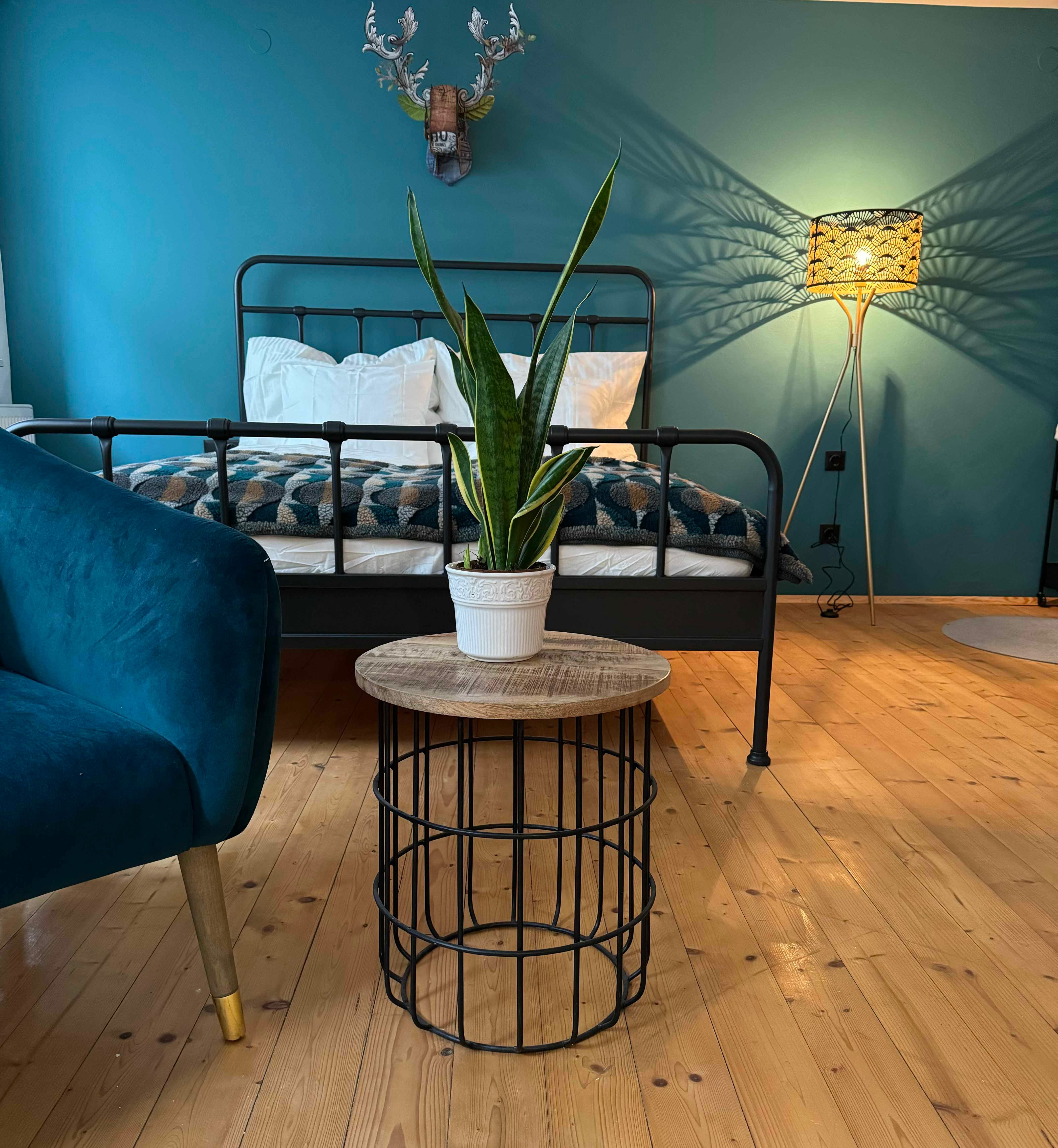 Bedroom with blue armchair, metal bed, plant on table and floor lamp.